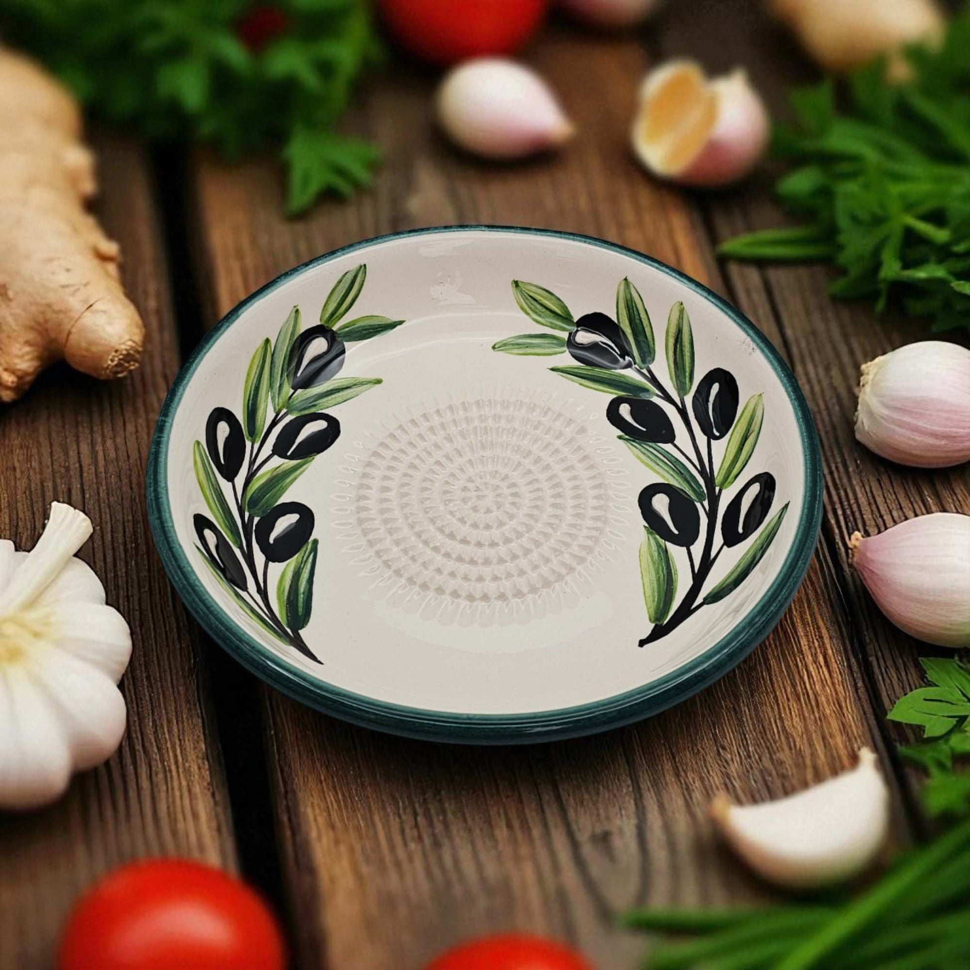 Decorative ceramic garlic grater bowl with olive design on a wooden surface with vegetables