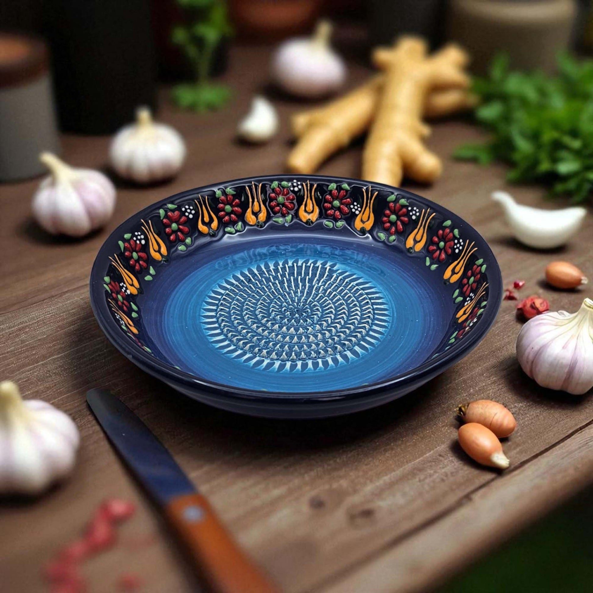 Decorative blue garlic grater bowl with floral patterns on a wooden table with garlic and ginger.