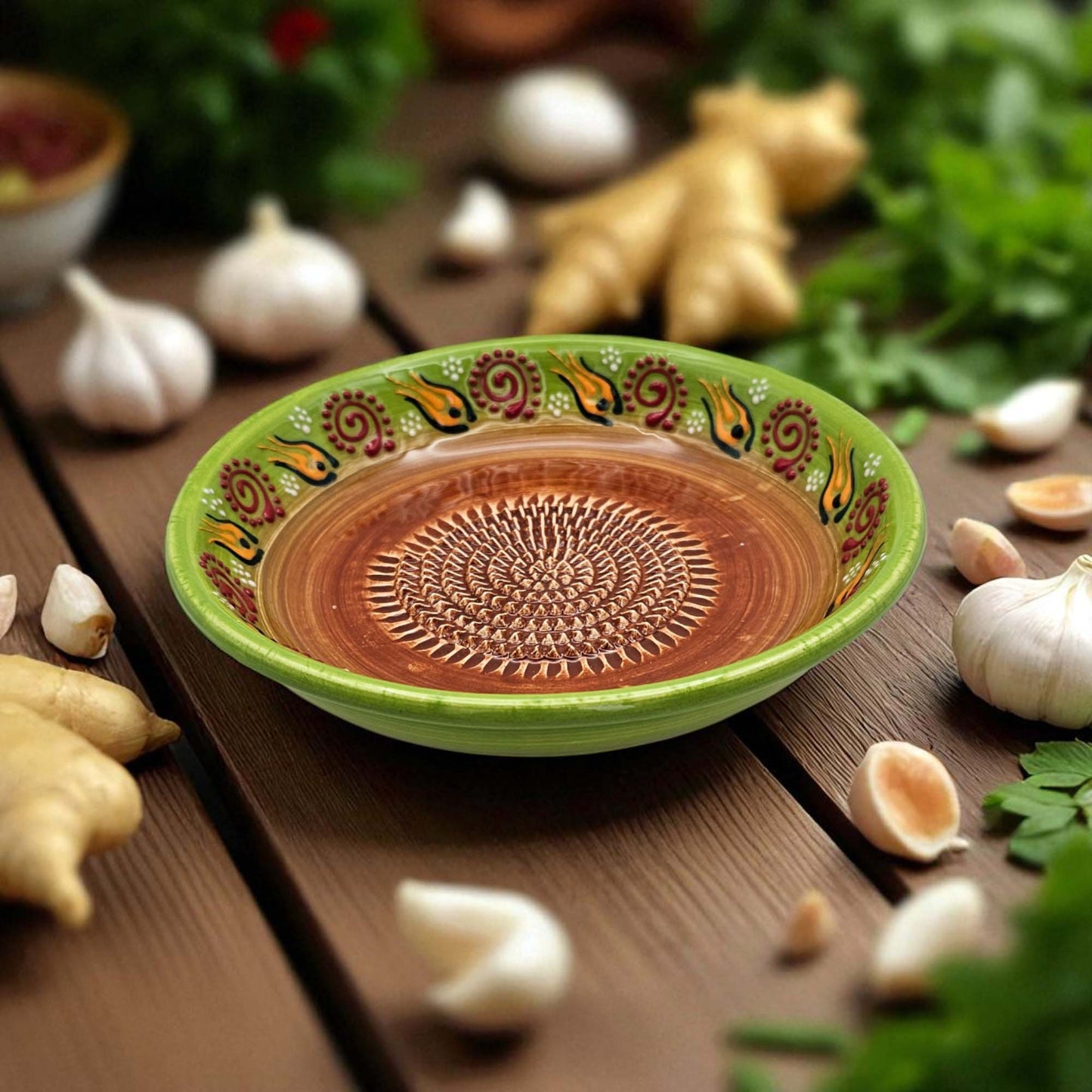 Decorative ceramic garlic grater bowl with a green rim on a wooden surface with garlic and ginger.