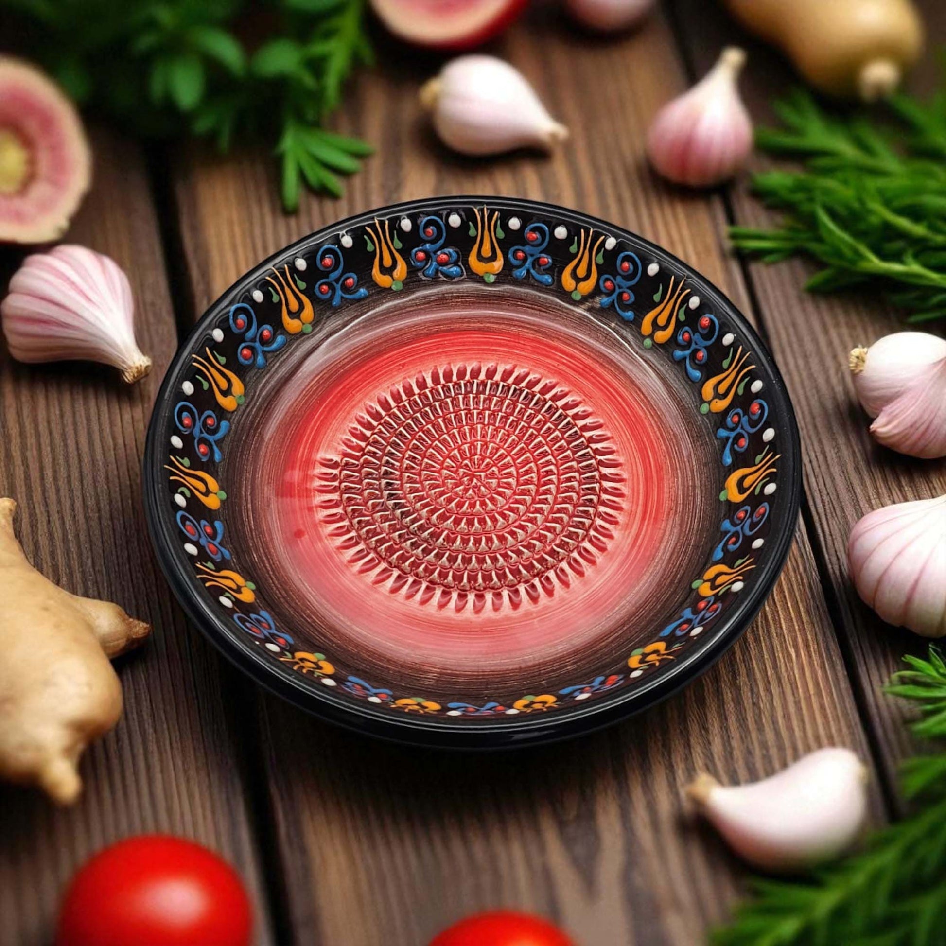 Decorative black garlic grater bowl with colorful patterns on a wooden surface with garlic and herbs.