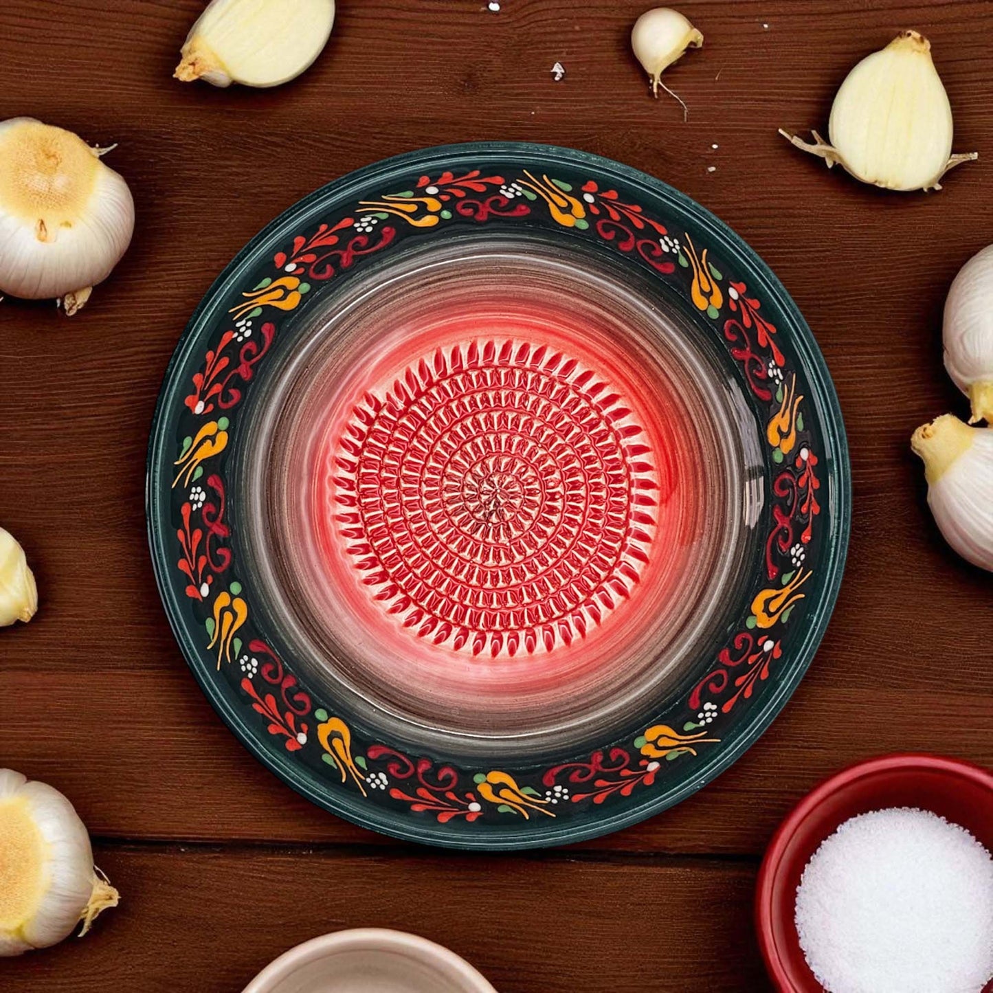 Decorative garlic grater bowl with colorful patterns on a wooden surface with garlic bulbs and a bowl of salt.