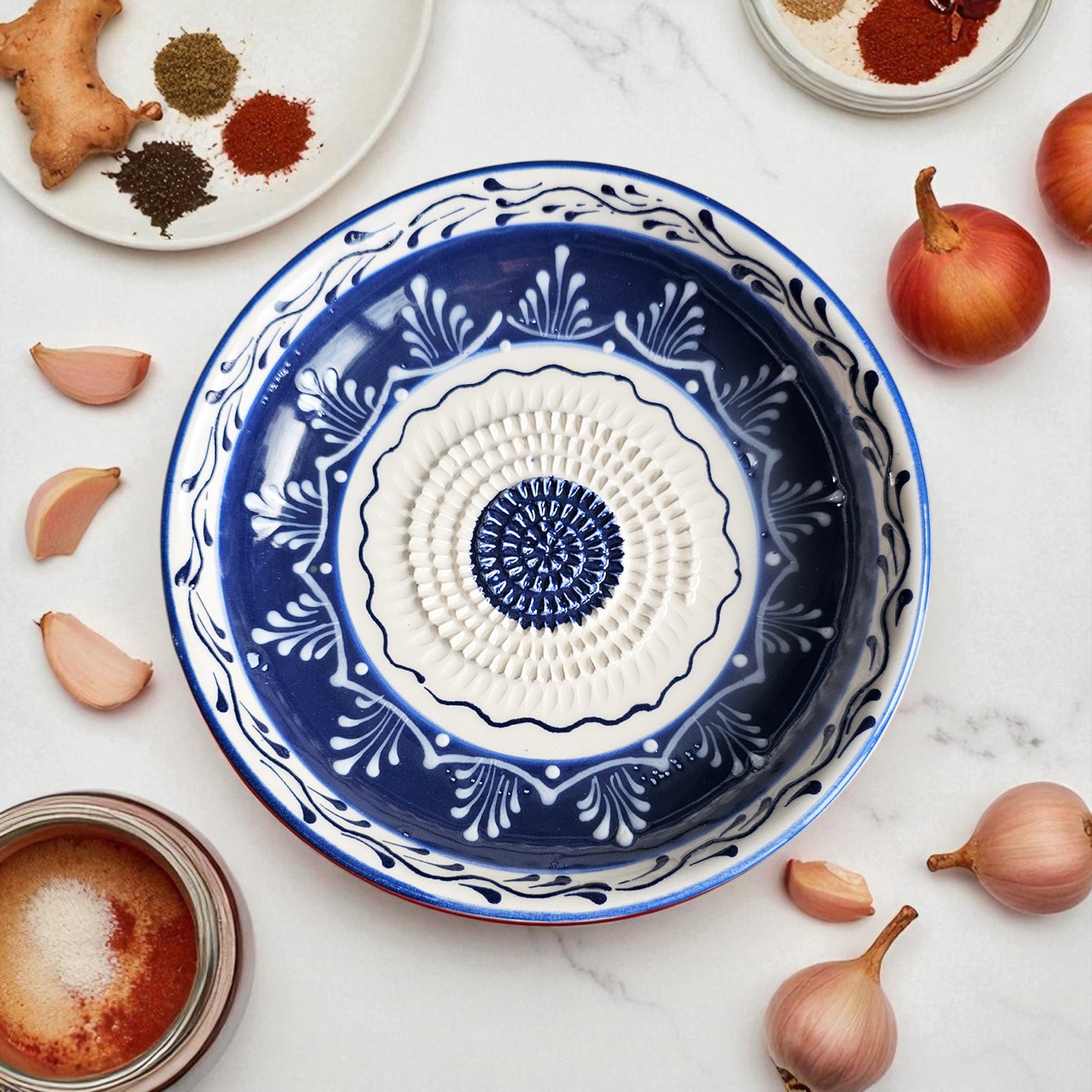 Decorative blue and white ceramic garlic grater bowl on a marble surface with ingredients around it.