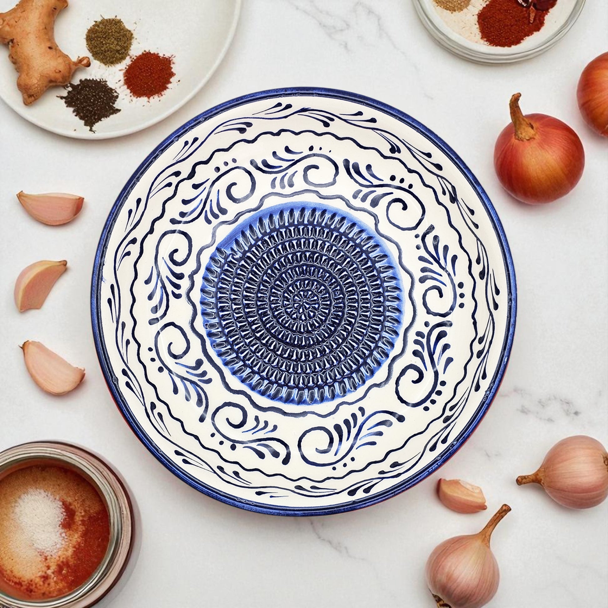 Decorative blue and white garlic grater bowl on a marble surface with ingredients around it.