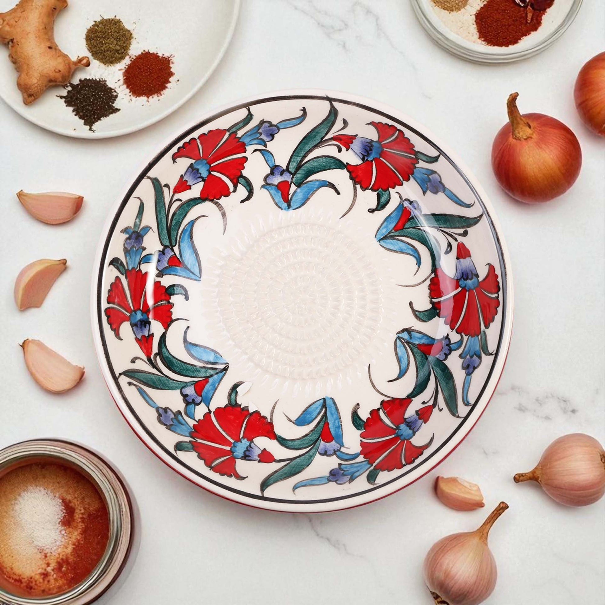 Decorative ceramic garlic grater bowl with floral patterns on a marble surface with ingredients.