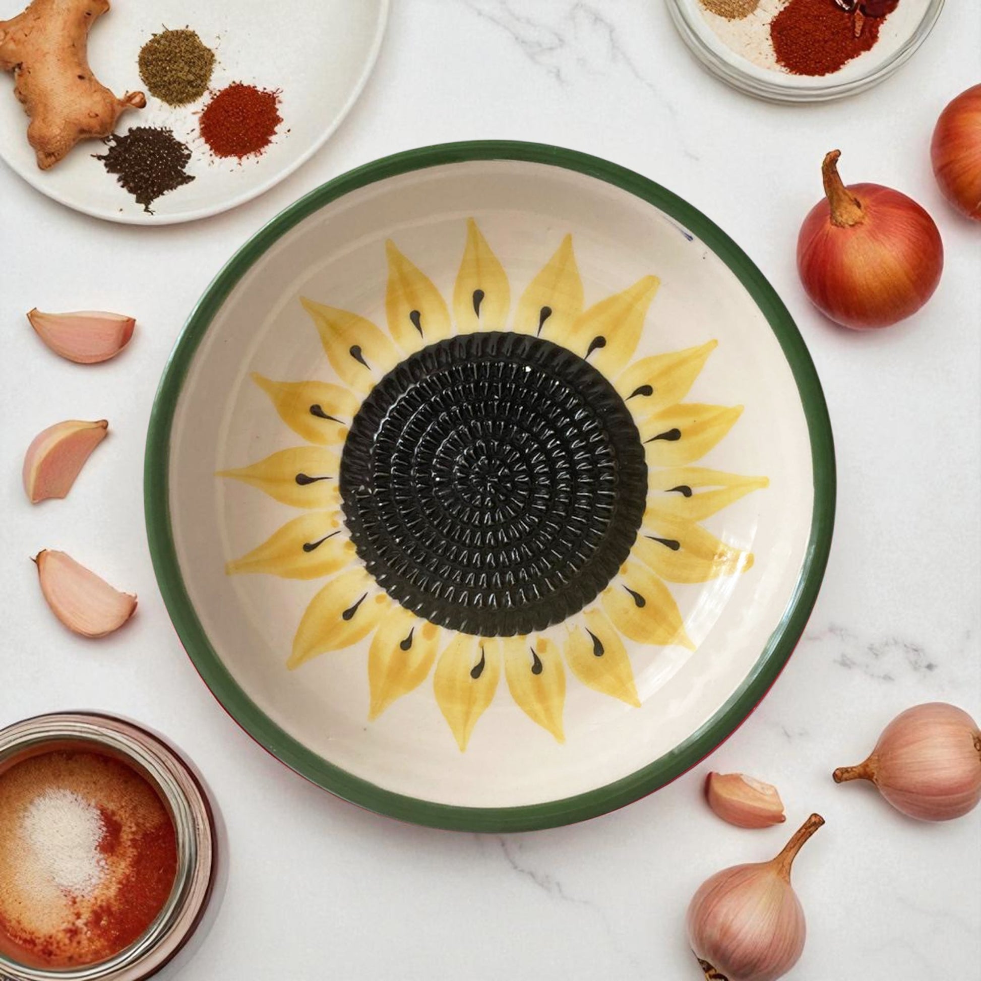 Ceramic garlic grater bowl with sunflower design on a marble surface with ingredients.