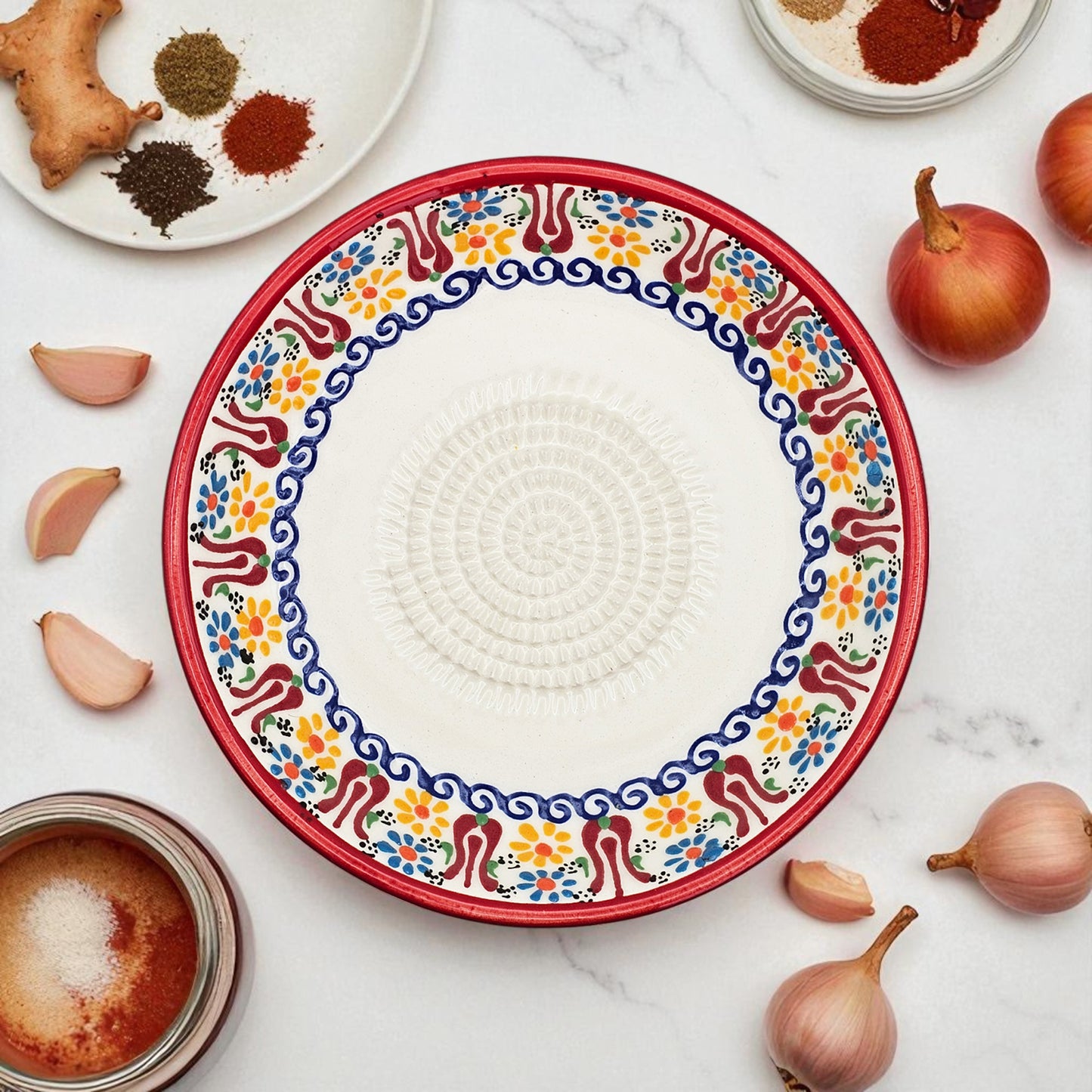 Decorative garlic grater bowl with colorful pattern on a marble surface with ingredients.