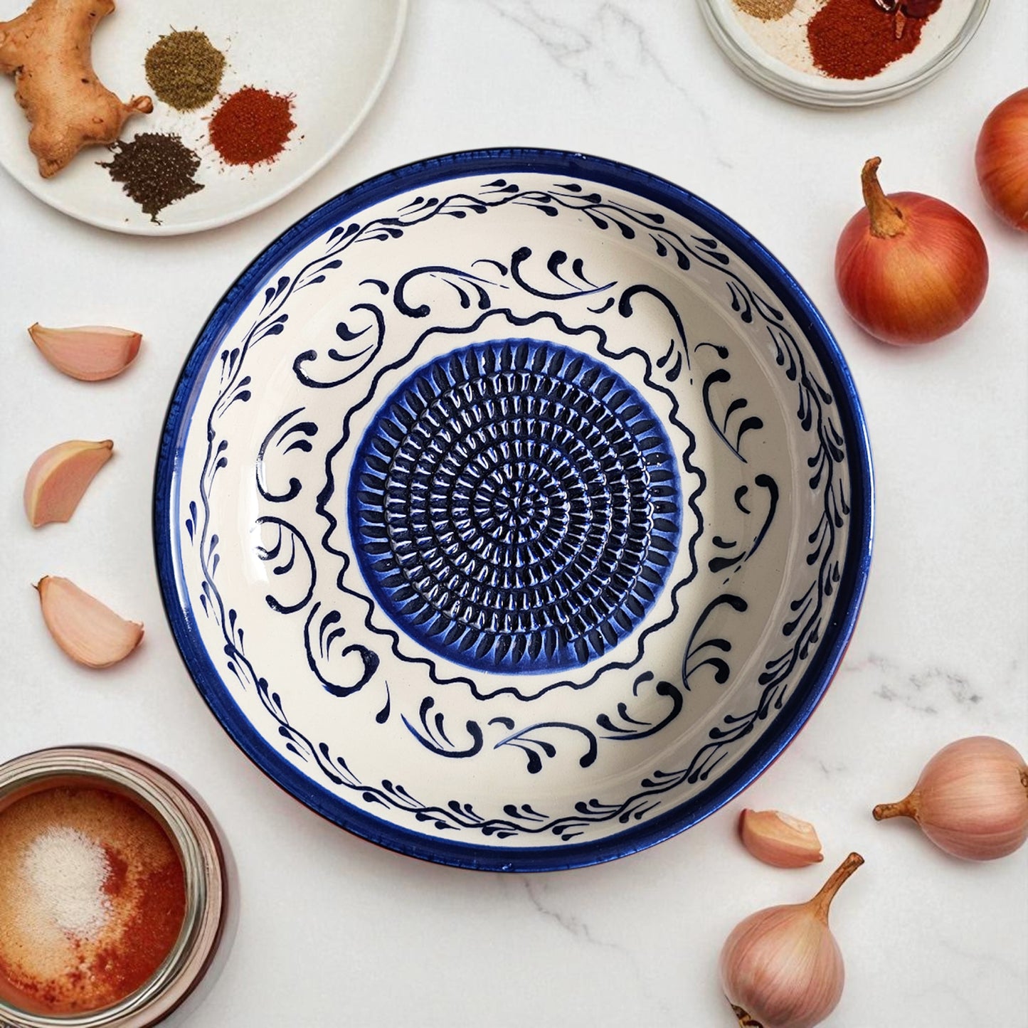Decorative ceramic garlic grater bowl with blue and white patterns on a marble surface with ingredients.