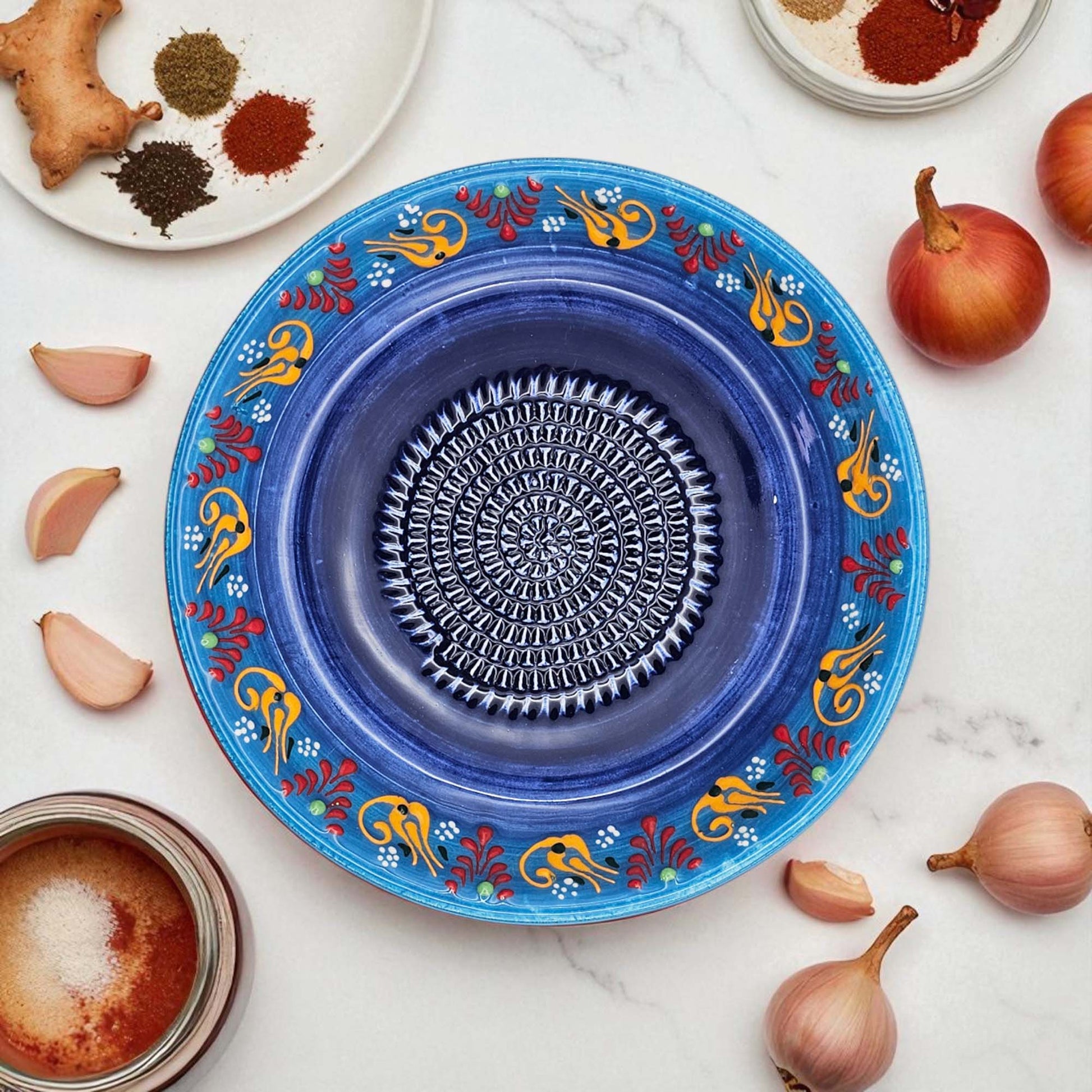 Blue decorative garlic grater bowl with colorful patterns on a white surface with ingredients.