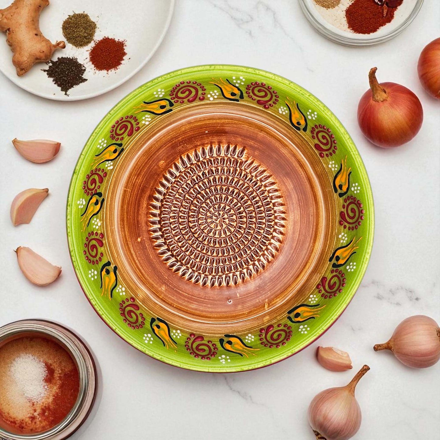 Decorative ceramic garlic grater bowl with green rim and brown center on a white surface with ingredients.