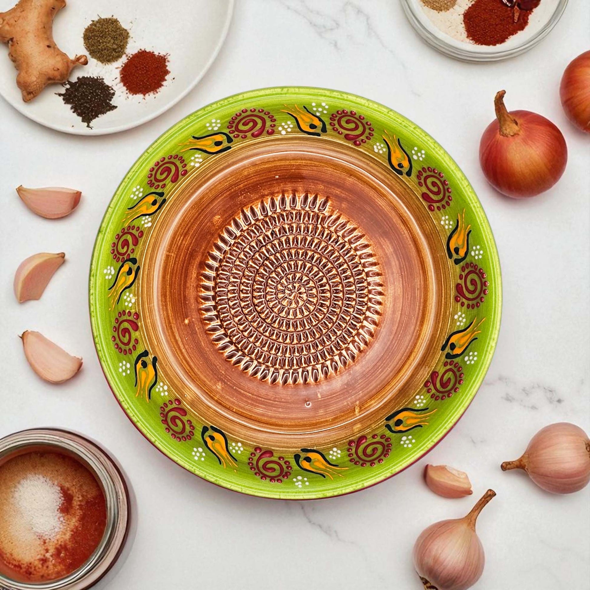 Decorative ceramic garlic grater bowl with green rim and brown center on a white surface with ingredients.