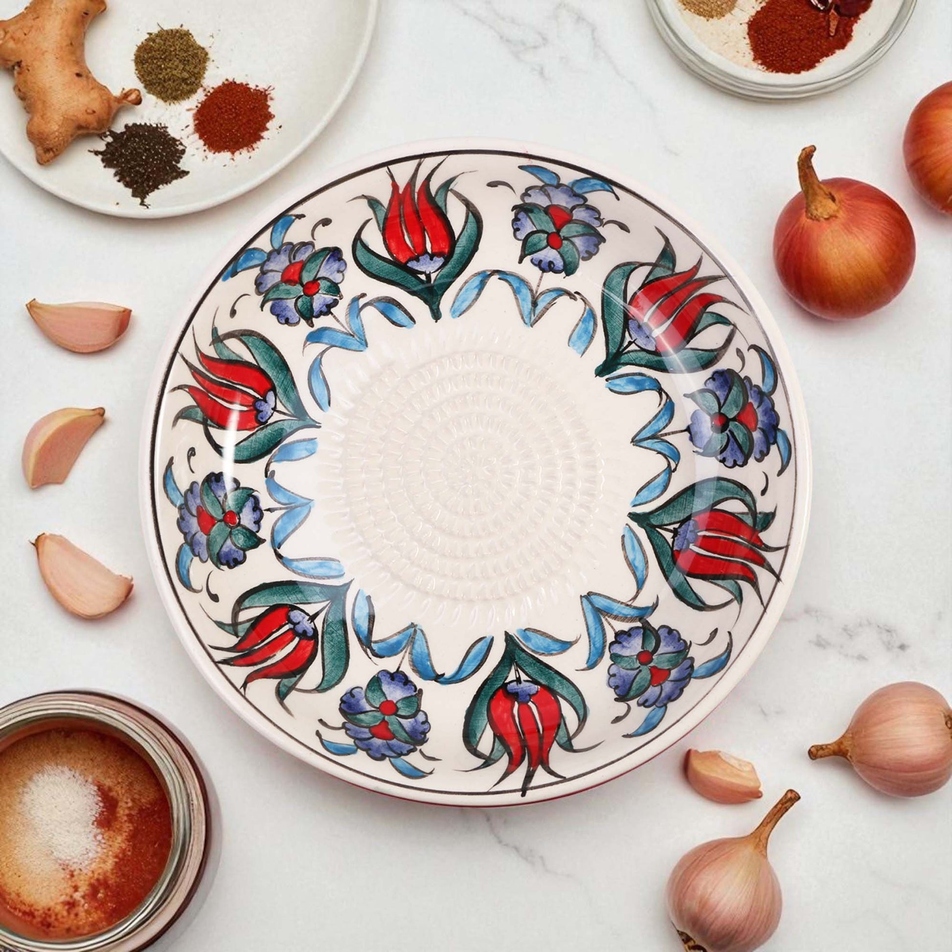 Decorative ceramic garlic grater bowl with floral patterns on a marble surface with ingredients.