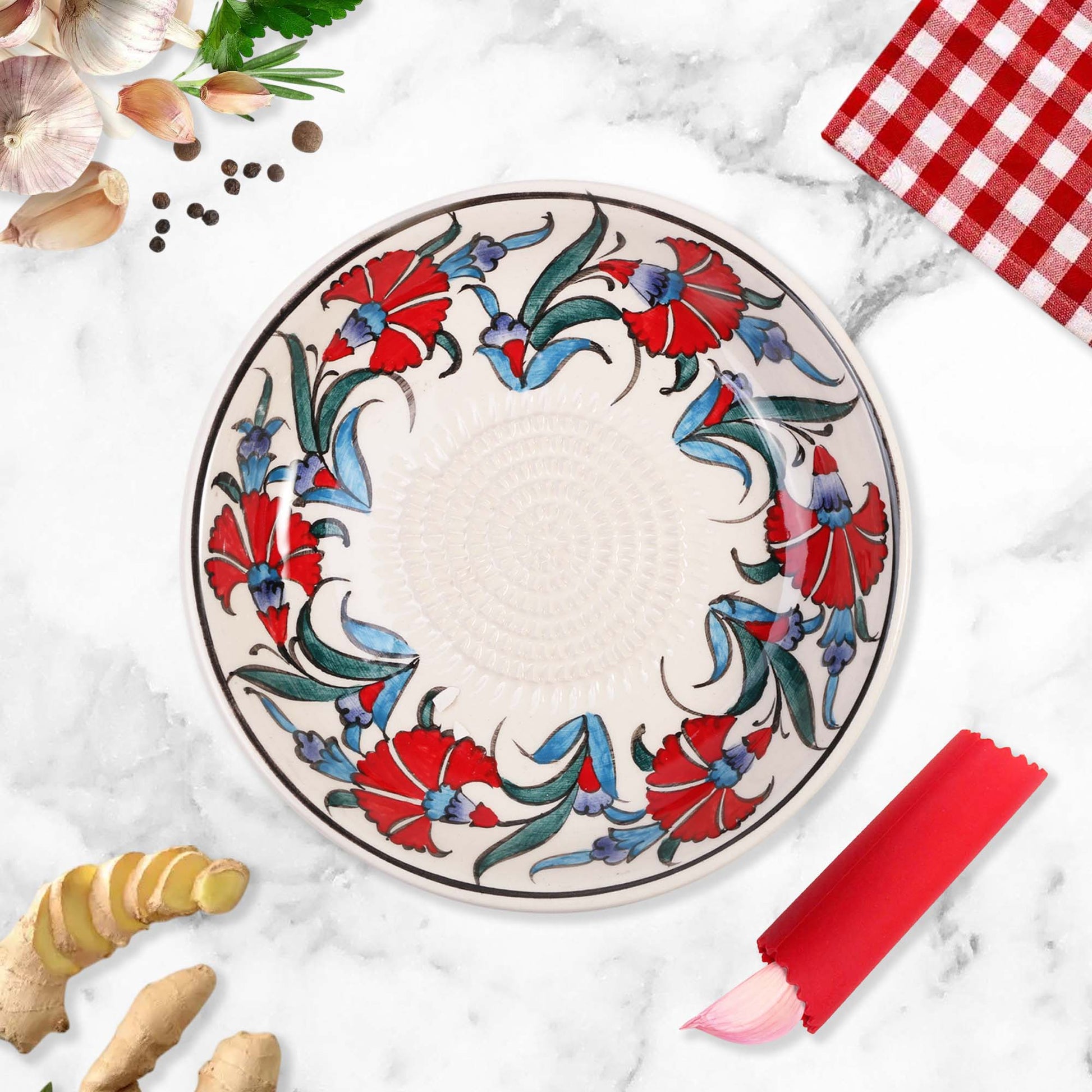 Decorative ceramic garlic grater bowl with floral design on a marble surface with kitchen items.