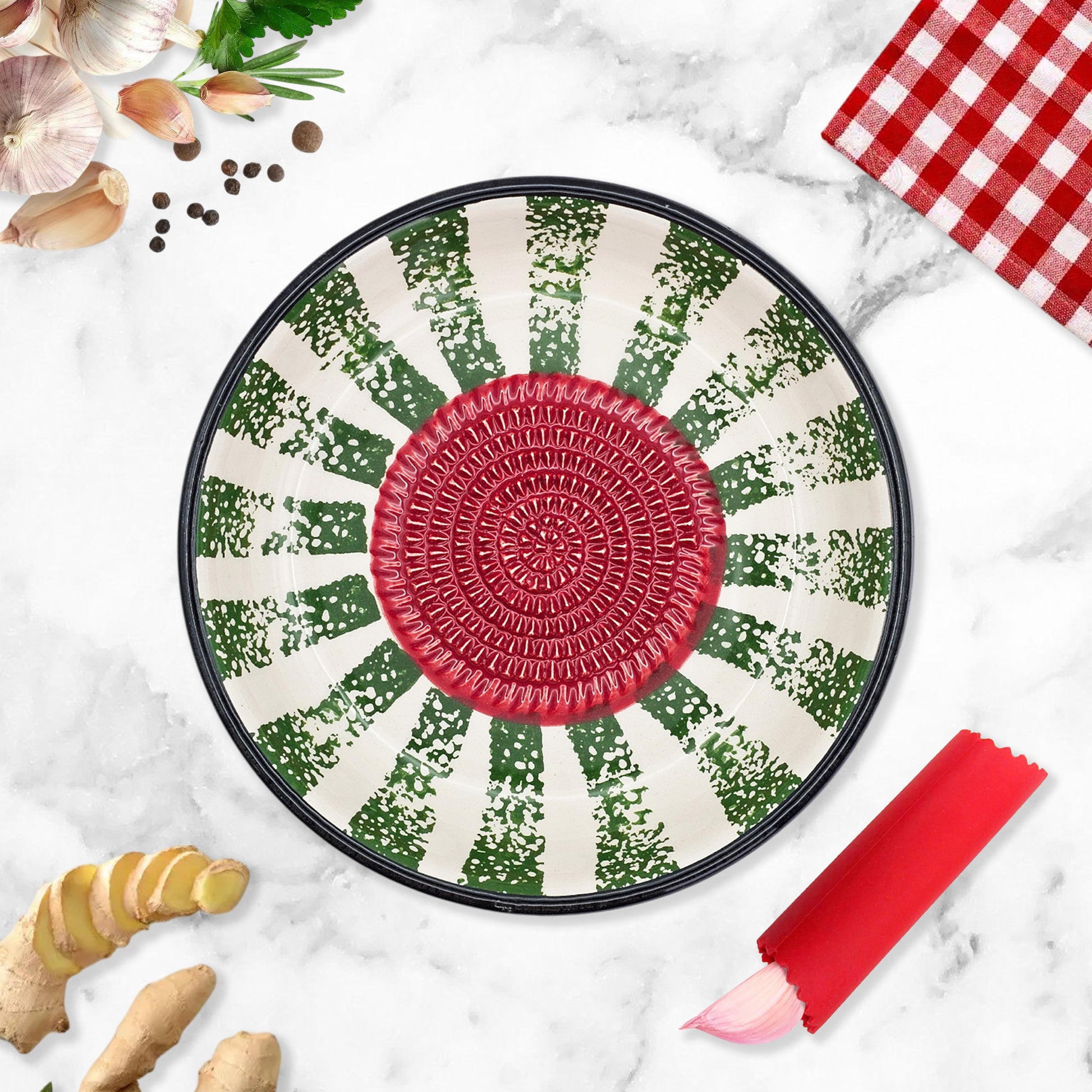 Decorative garlic grater bowl with a red center and green and white pattern on a marble surface with kitchen items.