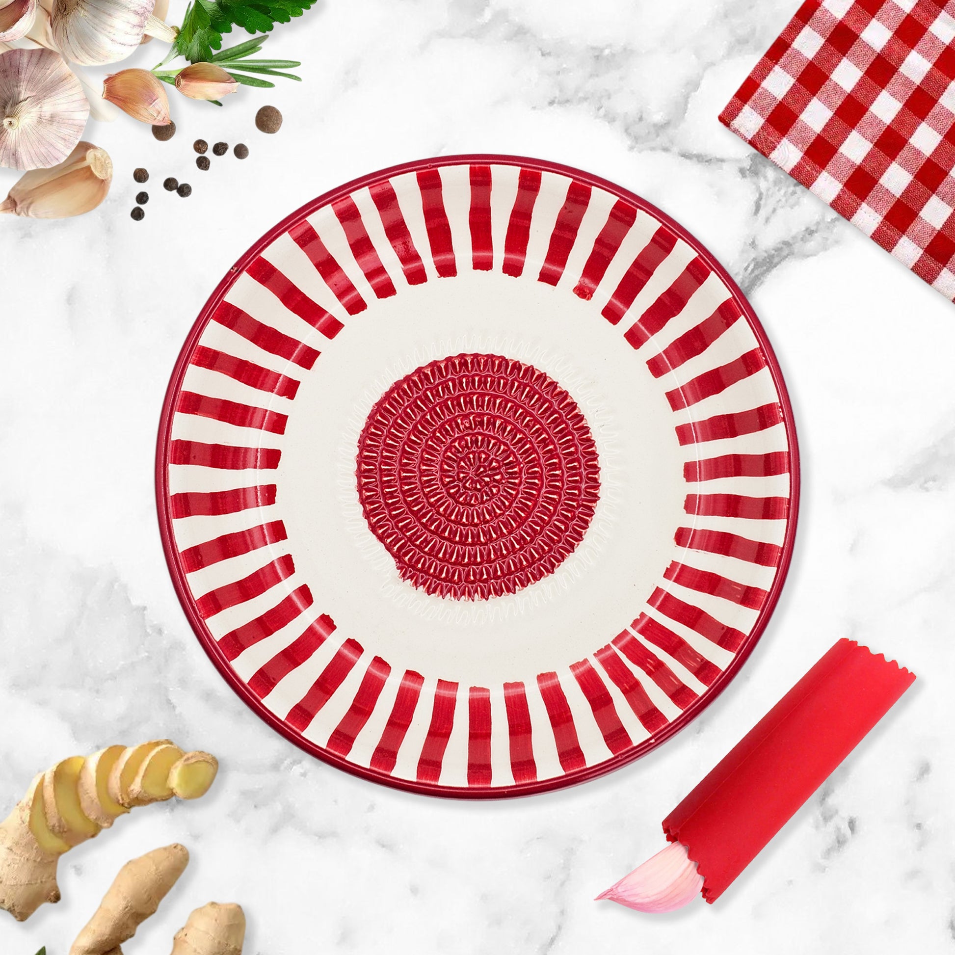 Red and white striped garlic grater bowl on a marble surface with ginger and a checkered cloth.