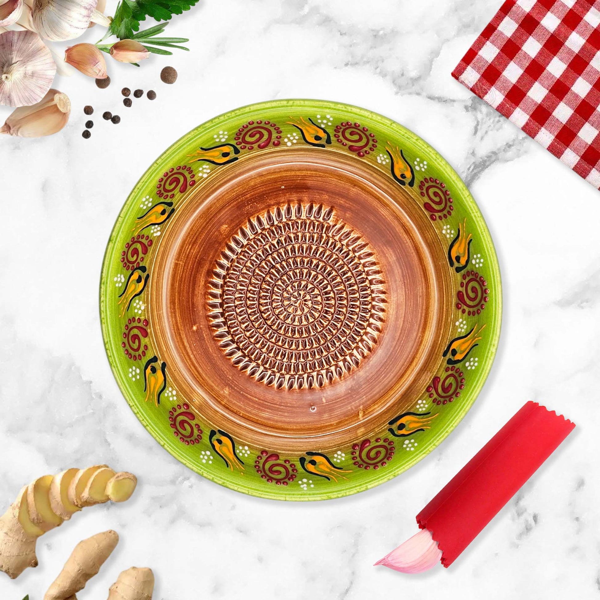 Decorative ceramic garlic grater bowl with green rim and brown center on a marble surface with kitchen items.