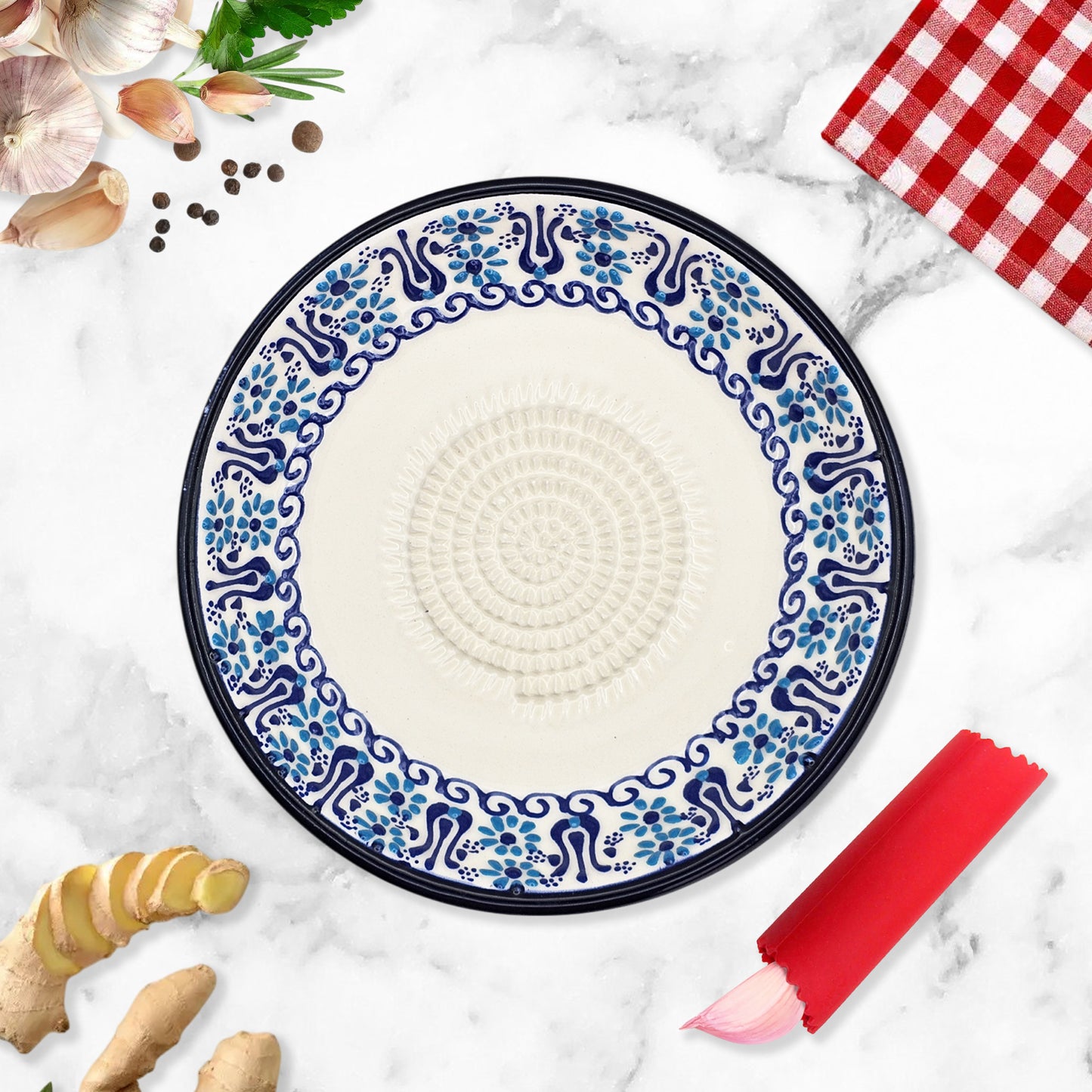 Decorative garlic grater plate with blue floral pattern on a marble surface with ginger and a red checkered cloth.