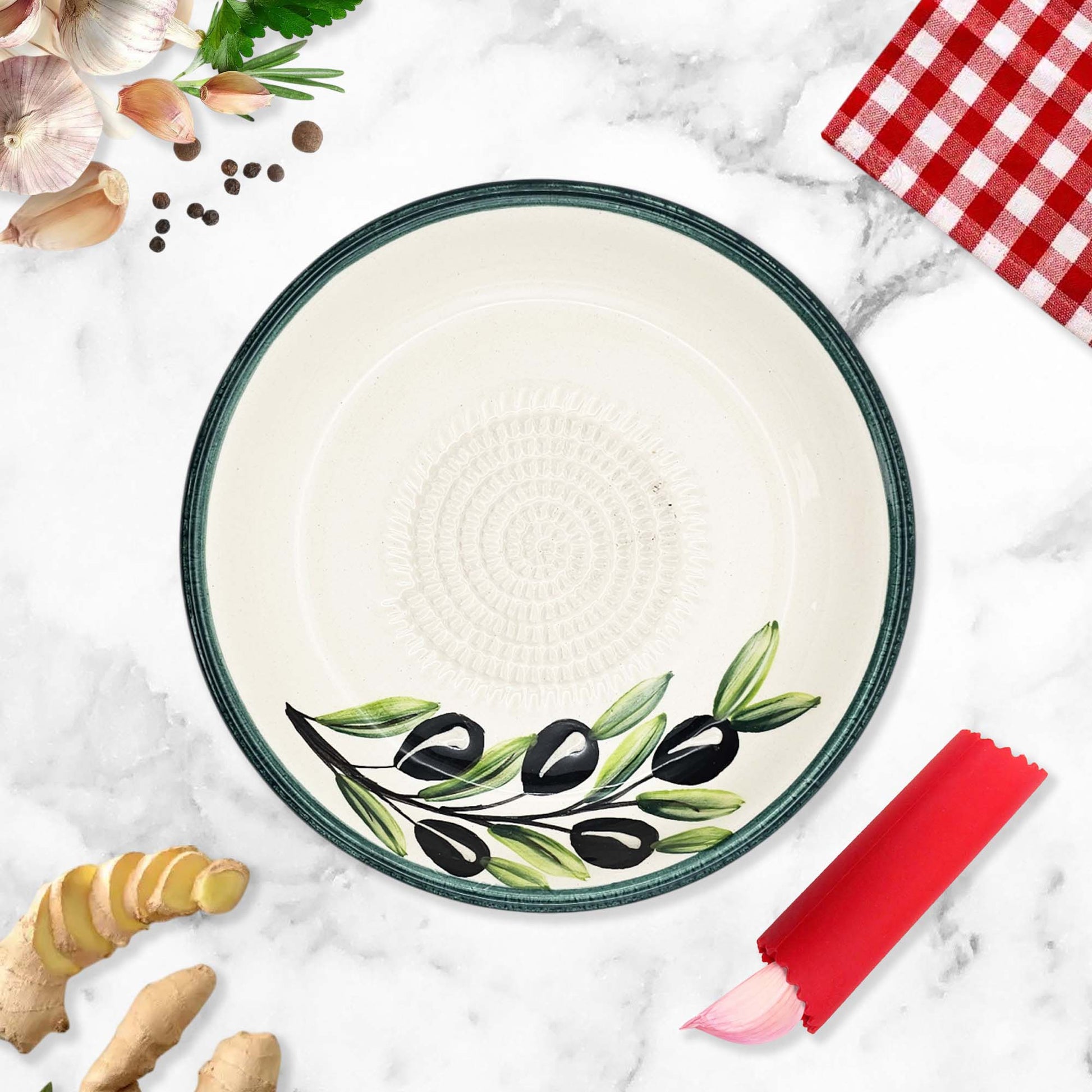 Ceramic garlic grater bowl with olive design on a marble surface with kitchen items.