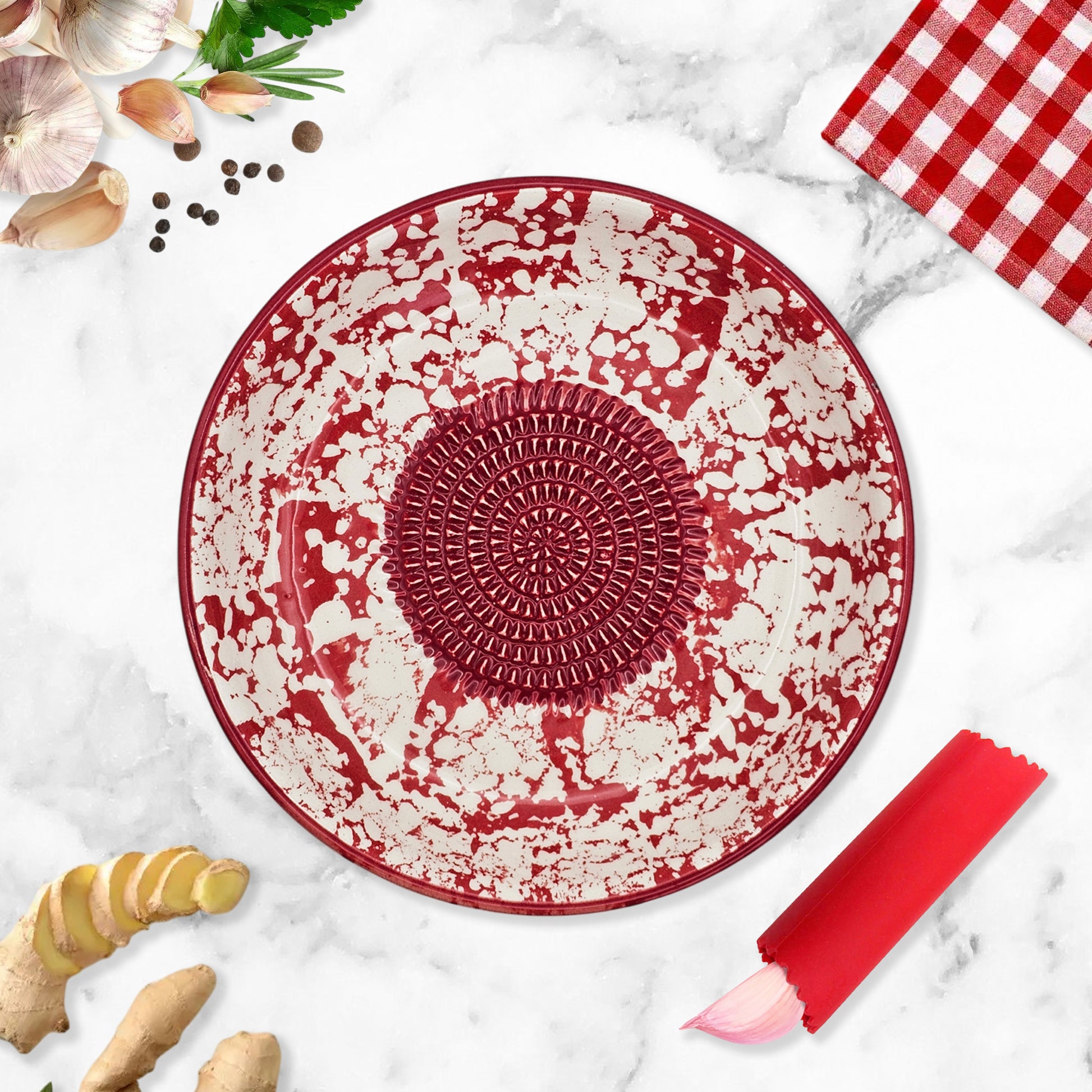 Red and white decorative garlic grater bowl on a marble surface with kitchen items around