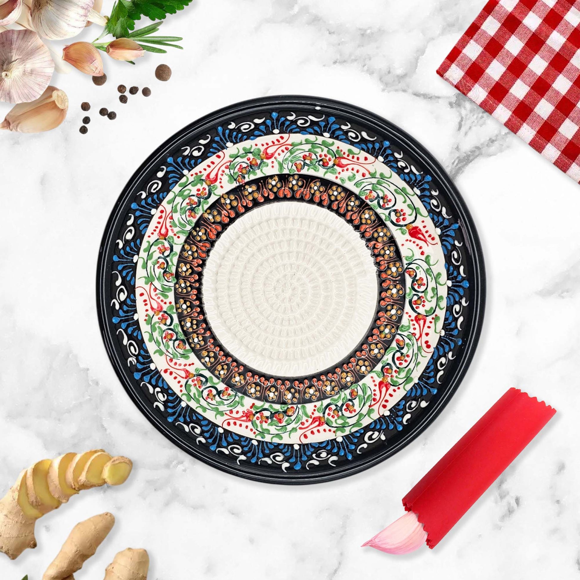 Decorative garlic grater bowl with floral patterns on a marble surface with kitchen items.
