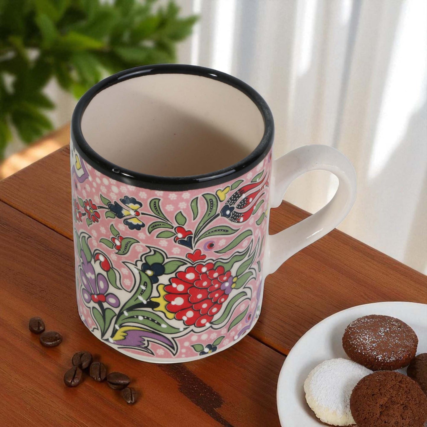 Decorative mug with floral pattern on a wooden table with cookies and coffee beans.
