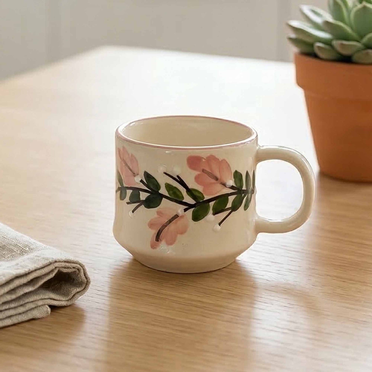 White mug with floral design on a wooden table next to a potted plant