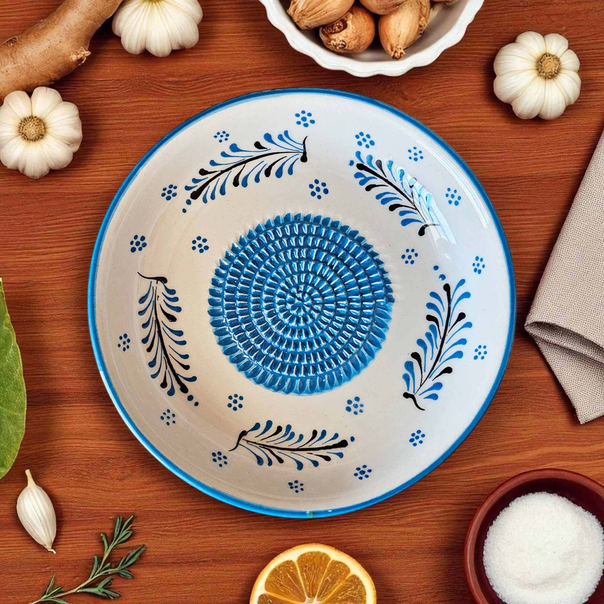 Decorative ceramic garlic grater bowl with blue and black patterns on a wooden surface with ingredients.