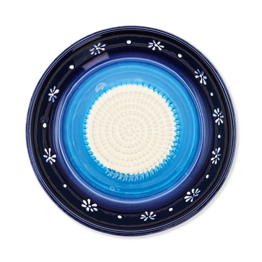 Blue ceramic garlic grater bowl with white floral patterns on a white background