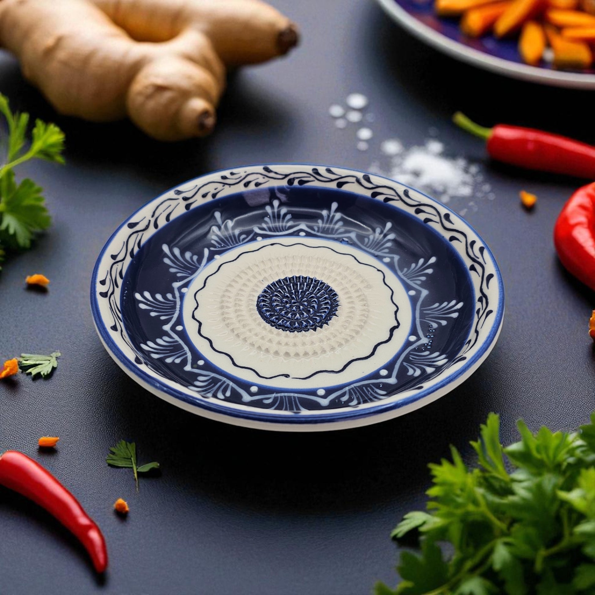 Decorative blue and white garlic grater bowl on a dark surface with spices and herbs around