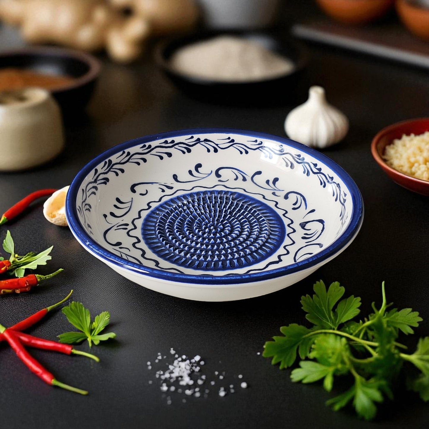 Decorative blue and white ceramic garlic grater bowl on a dark surface with herbs and spices.