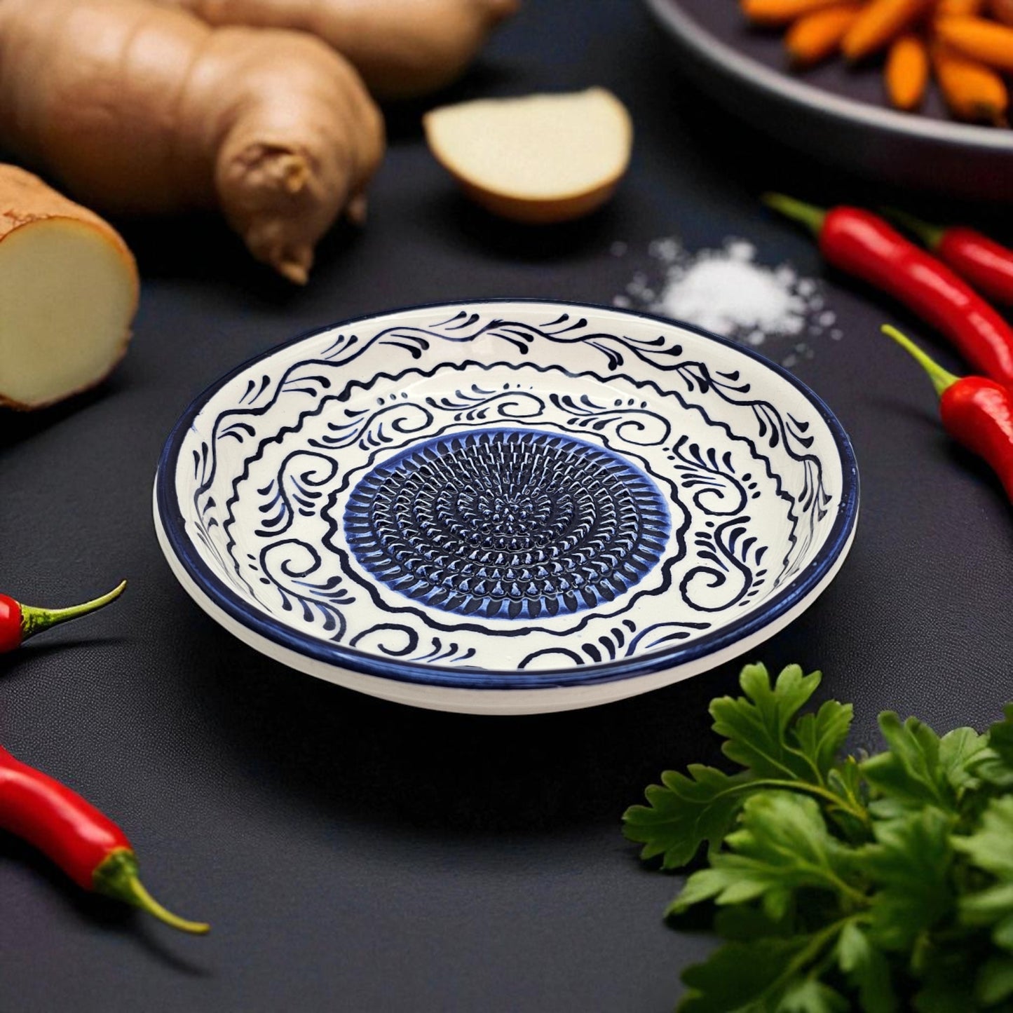 Decorative ceramic garlic grater bowl with blue center on a dark surface with vegetables