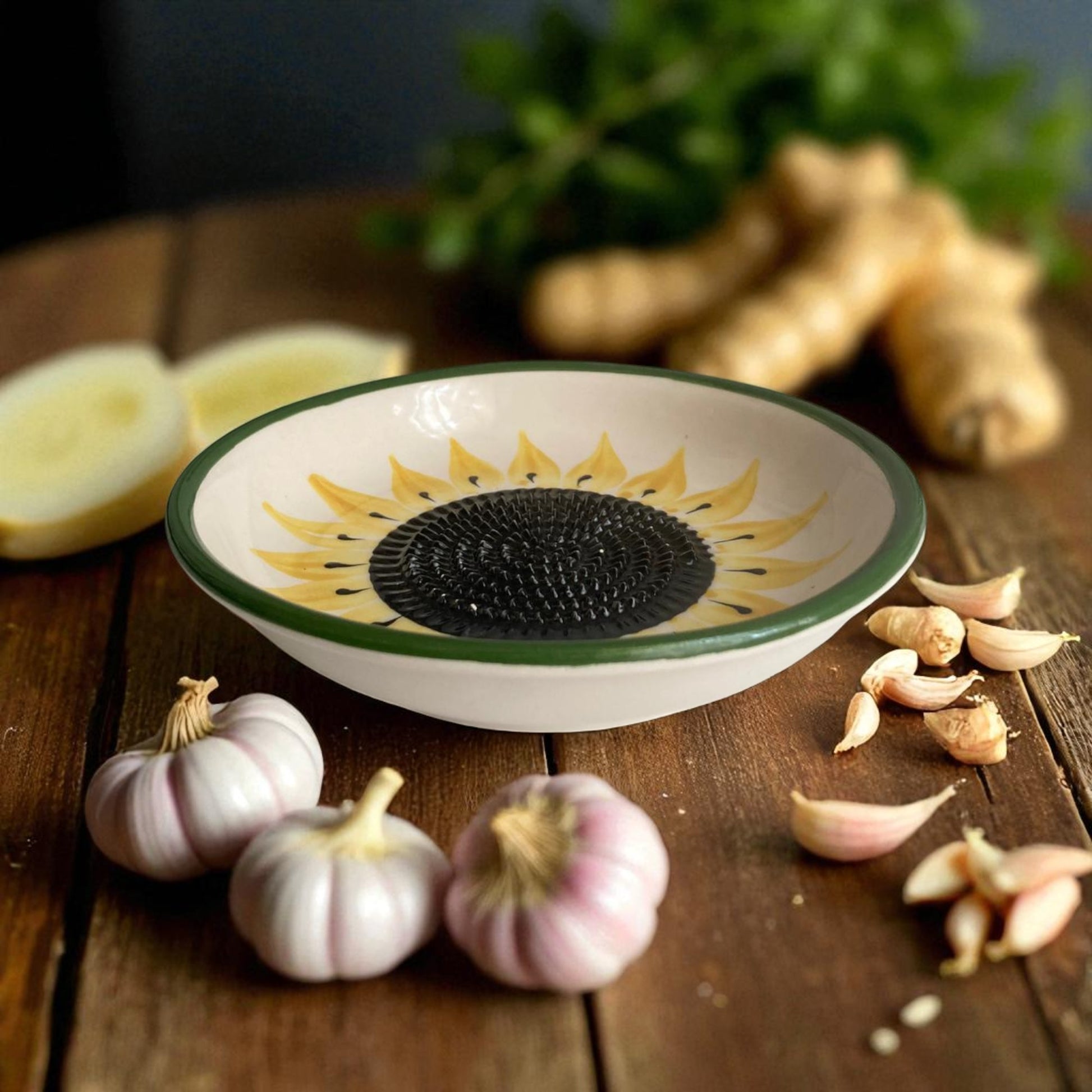 Decorative sunflower-patterned garlic grater bowl on a wooden surface with garlic and ginger.