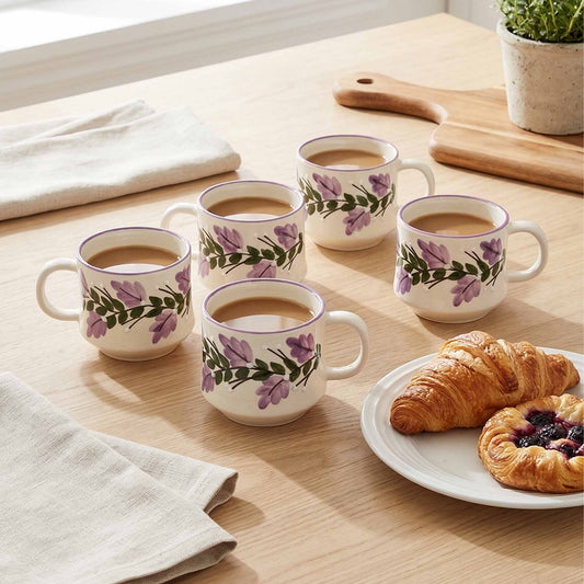 Set of six floral mugs with coffee on a wooden table with pastries.
