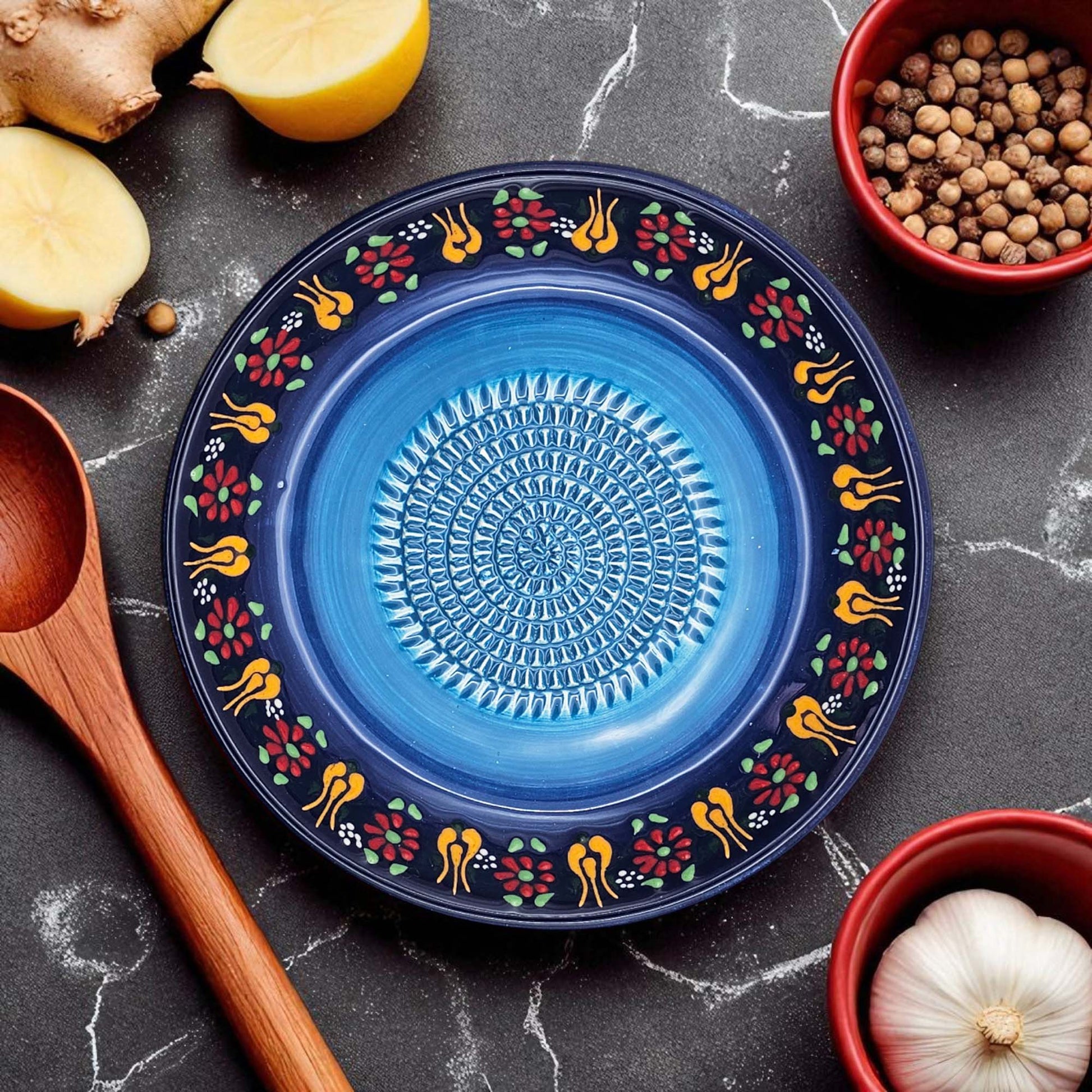 Blue decorative garlic grater bowl with floral patterns on a dark surface with kitchen items.