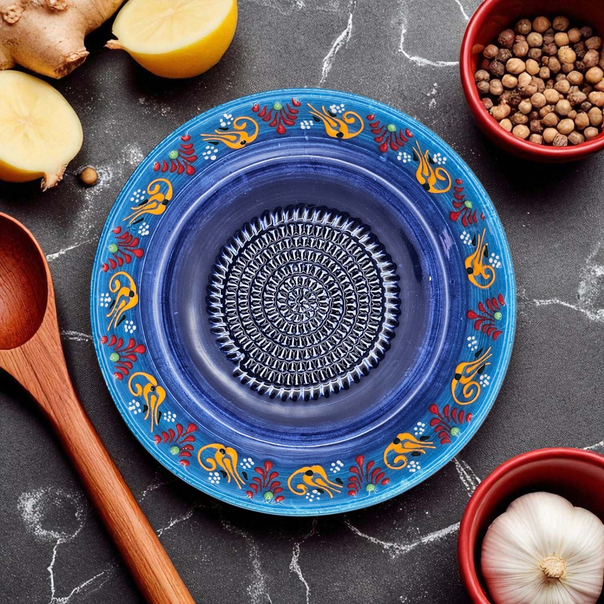 Decorative blue garlic grater bowl with floral patterns on a dark surface with kitchen items.
