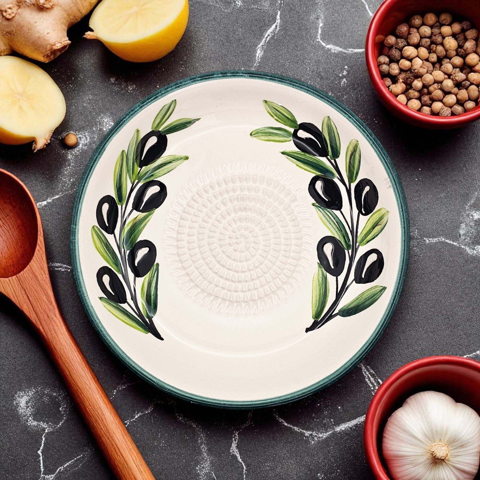 Decorative garlic grater bowl with olive design on a kitchen counter with ingredients