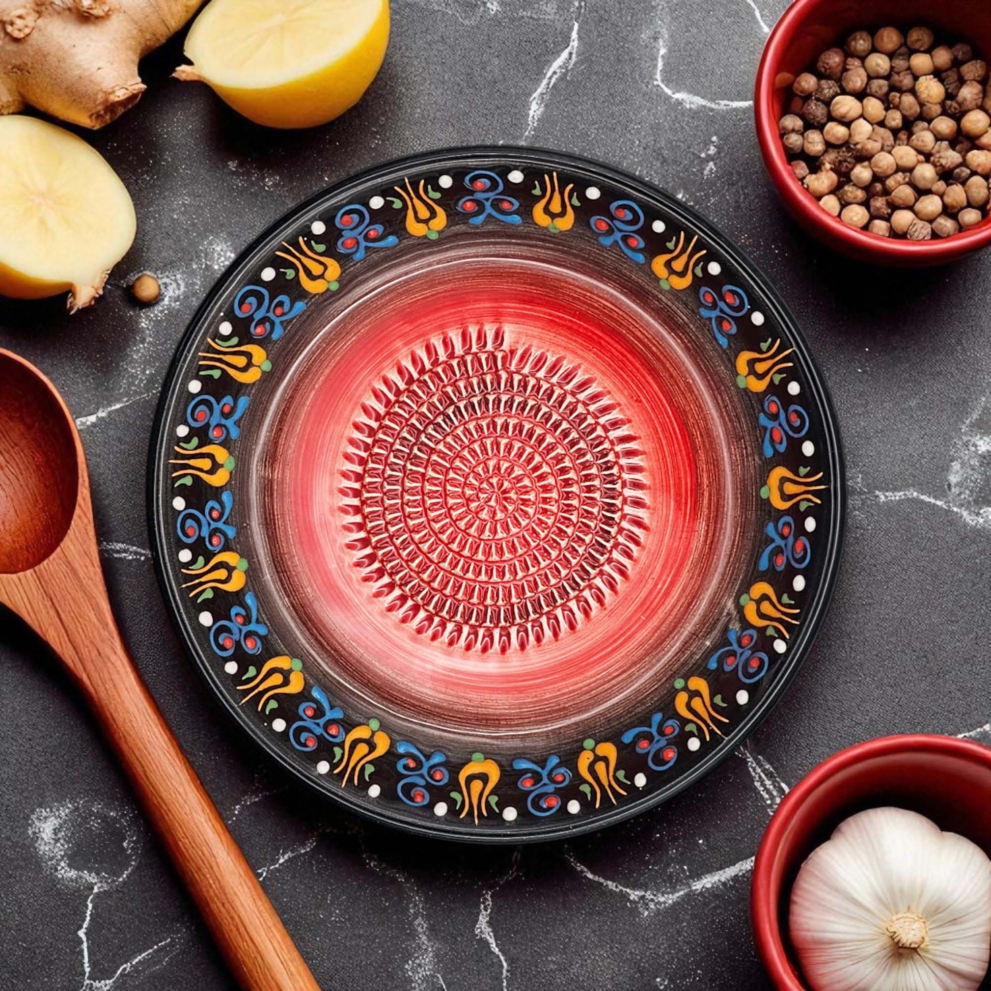 Decorative black garlic grater bowl with colorful patterns on a dark surface with kitchen items.