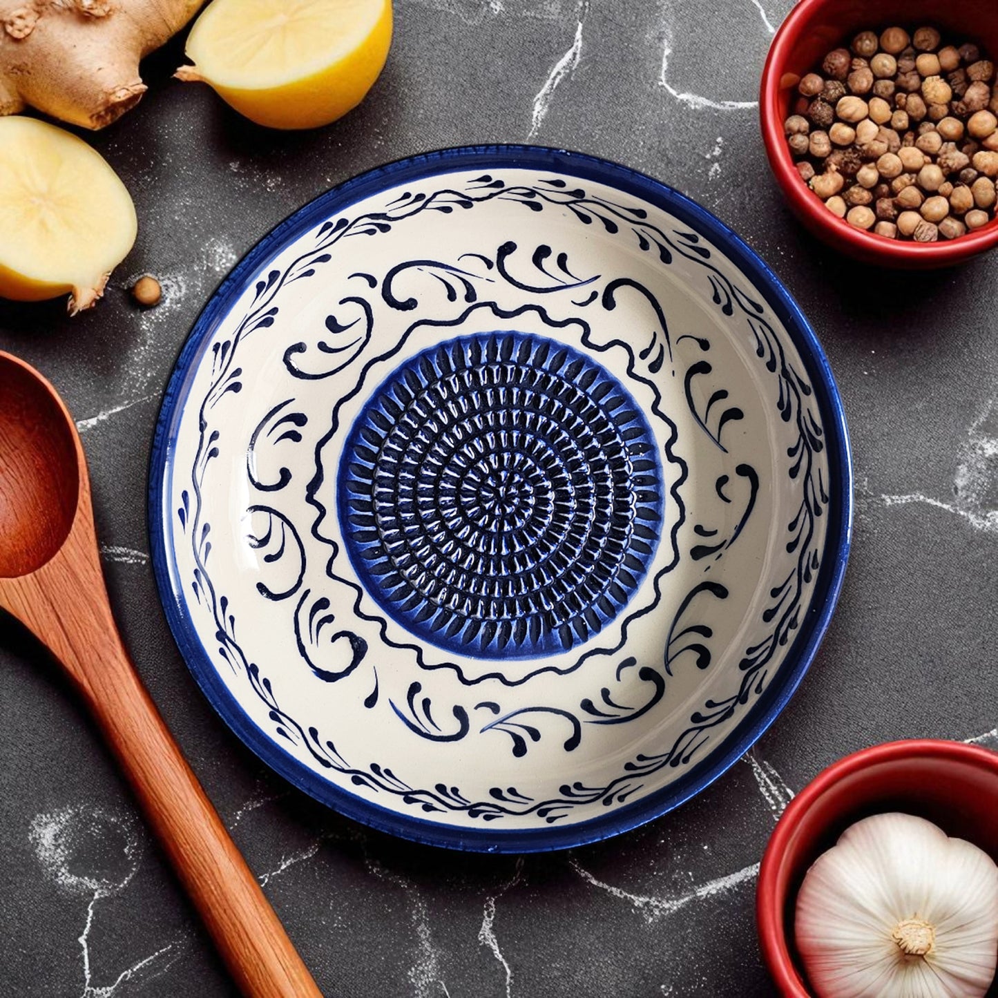 Decorative ceramic garlic grater bowl with blue and white pattern on a dark surface with kitchen items.
