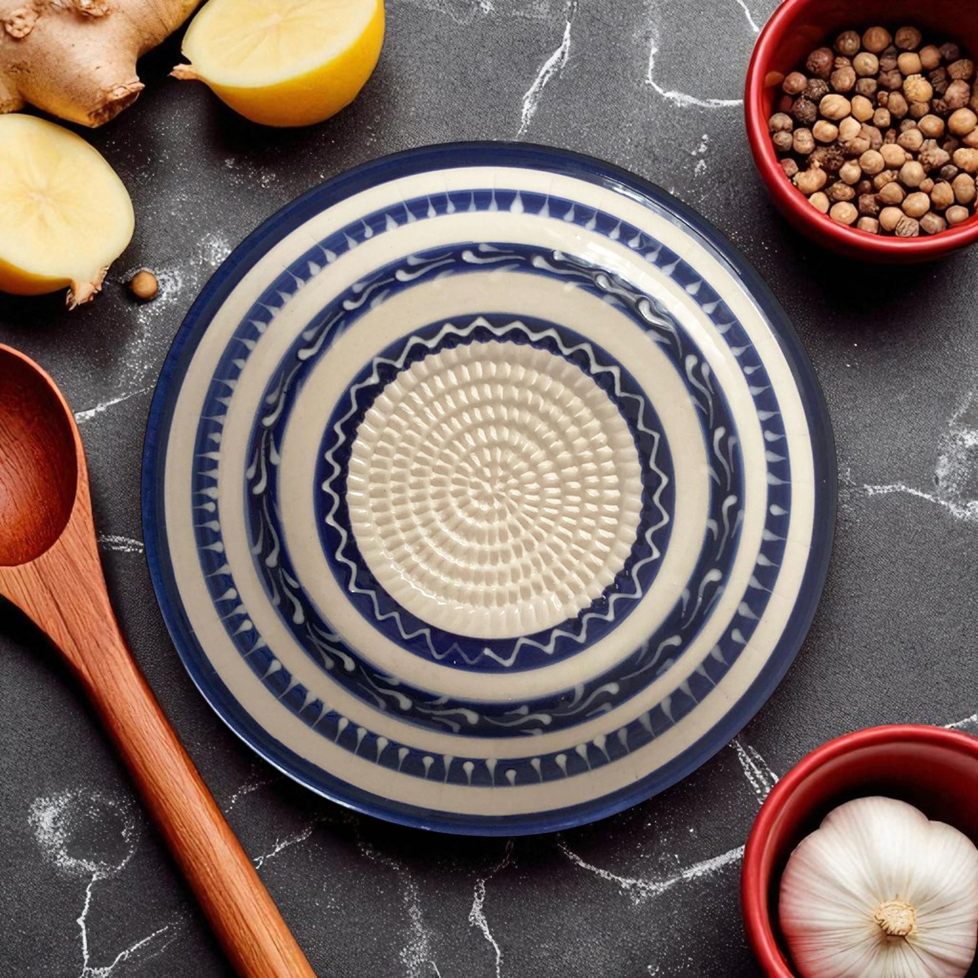 Blue and white ceramic garlic grater bowl with geometric pattern on a dark surface with ingredients.