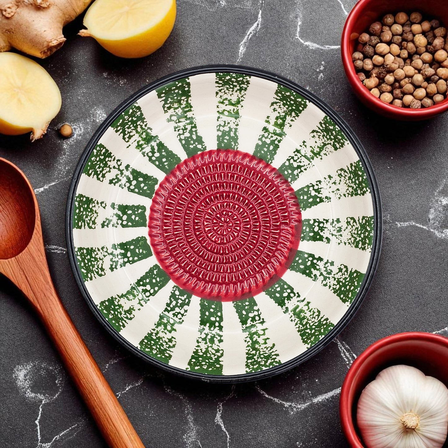 Decorative garlic grater bowl with a red center and green and white pattern on a dark surface with kitchen items.