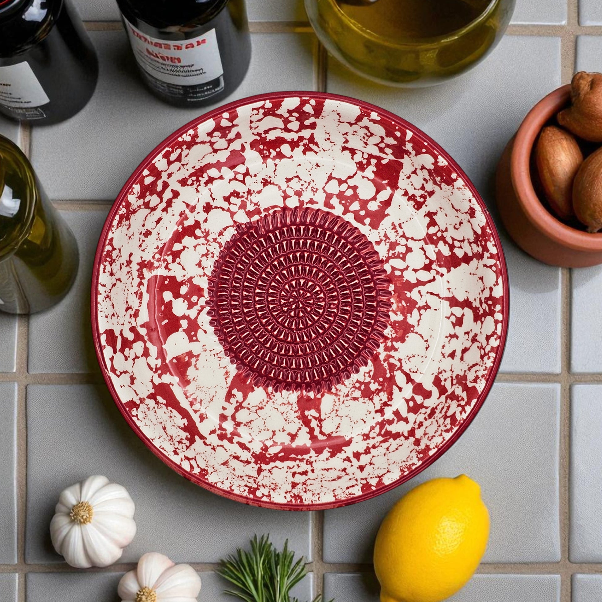 Red and white ceramic garlic grater bowl on a tiled surface with lemons and herbs.