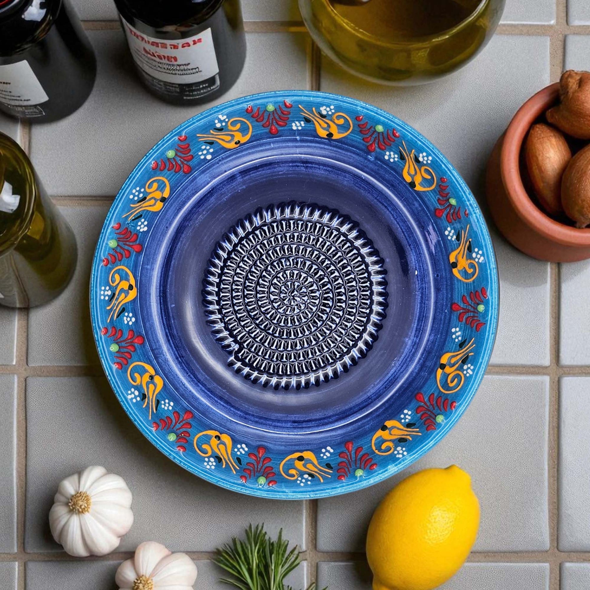Blue decorative garlic grater bowl with colorful patterns on a tiled surface with ingredients.