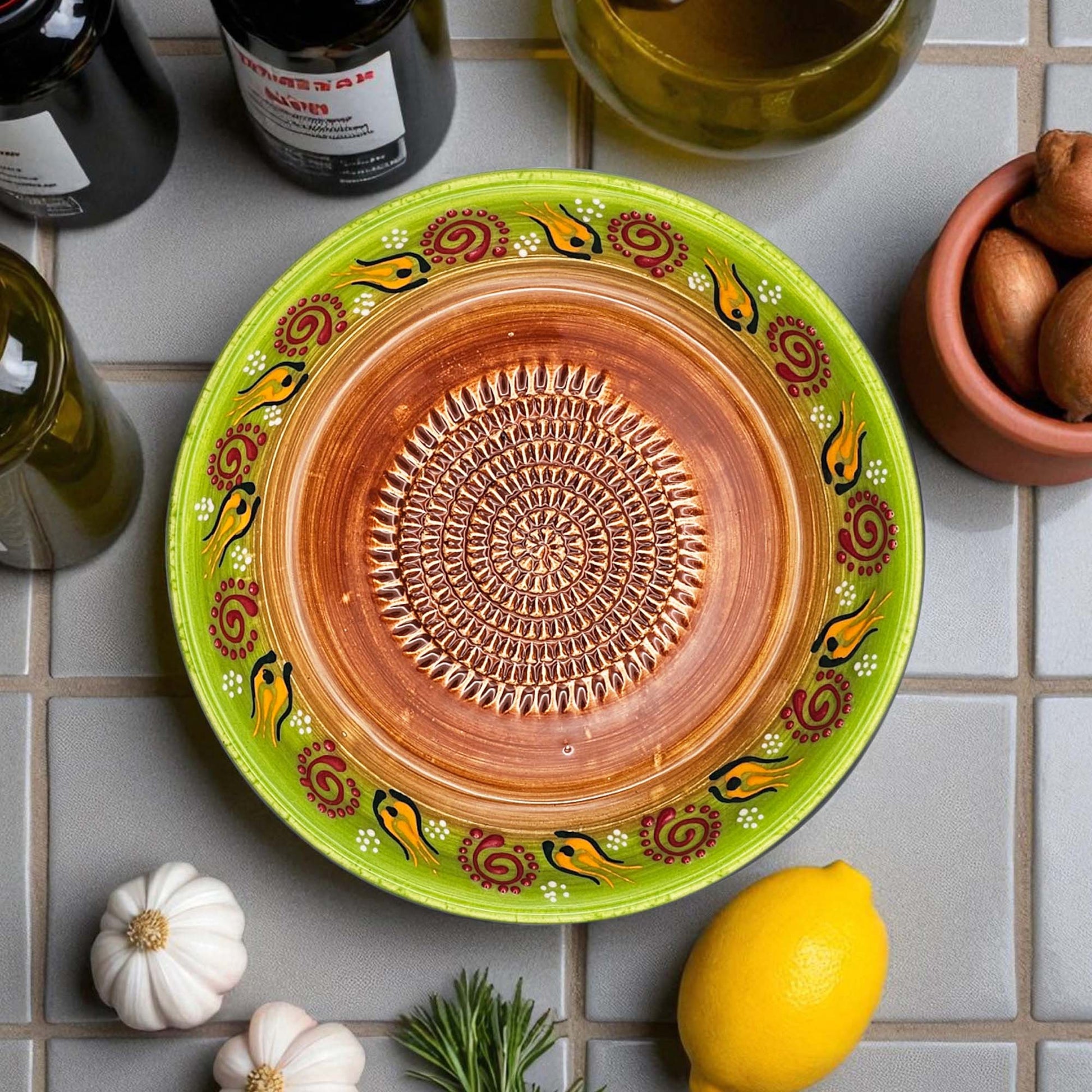 Decorative ceramic garlic grater bowl with green rim and brown center on a tiled surface with lemons and garlic.