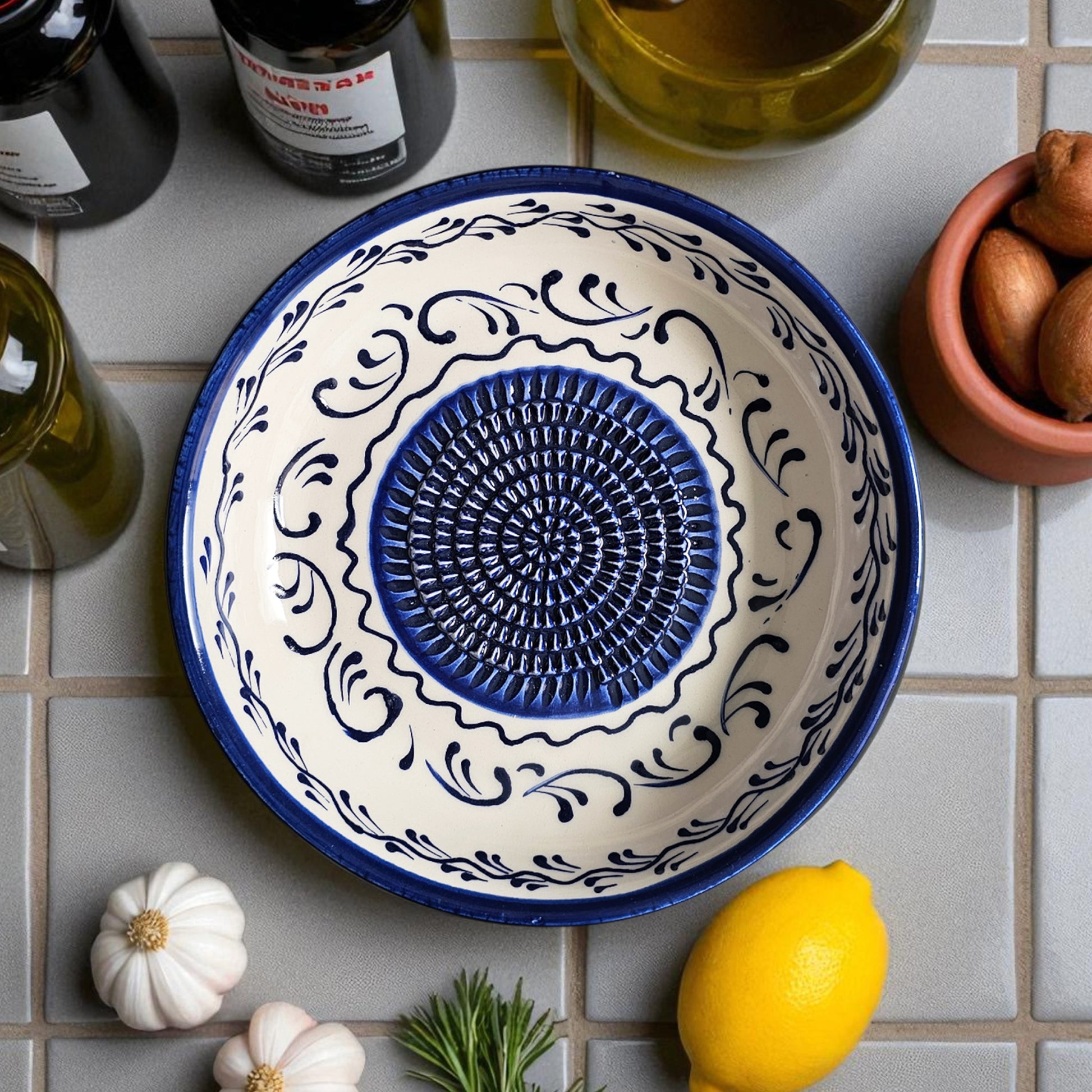 Decorative ceramic garlic grater bowl with blue center and white border on a tiled surface with lemons and garlic.