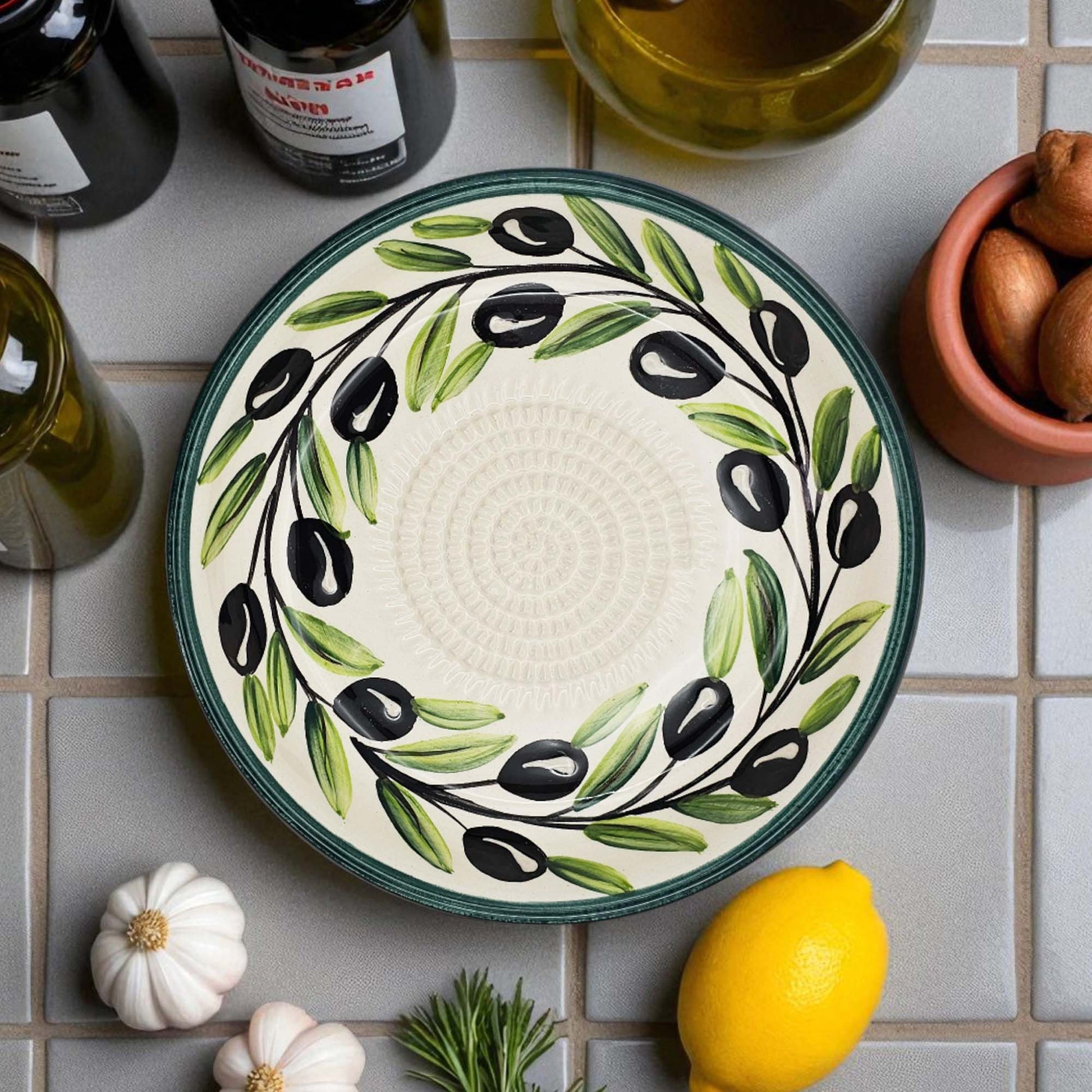 Ceramic garlic grater bowl with olive design on a tiled surface with ingredients