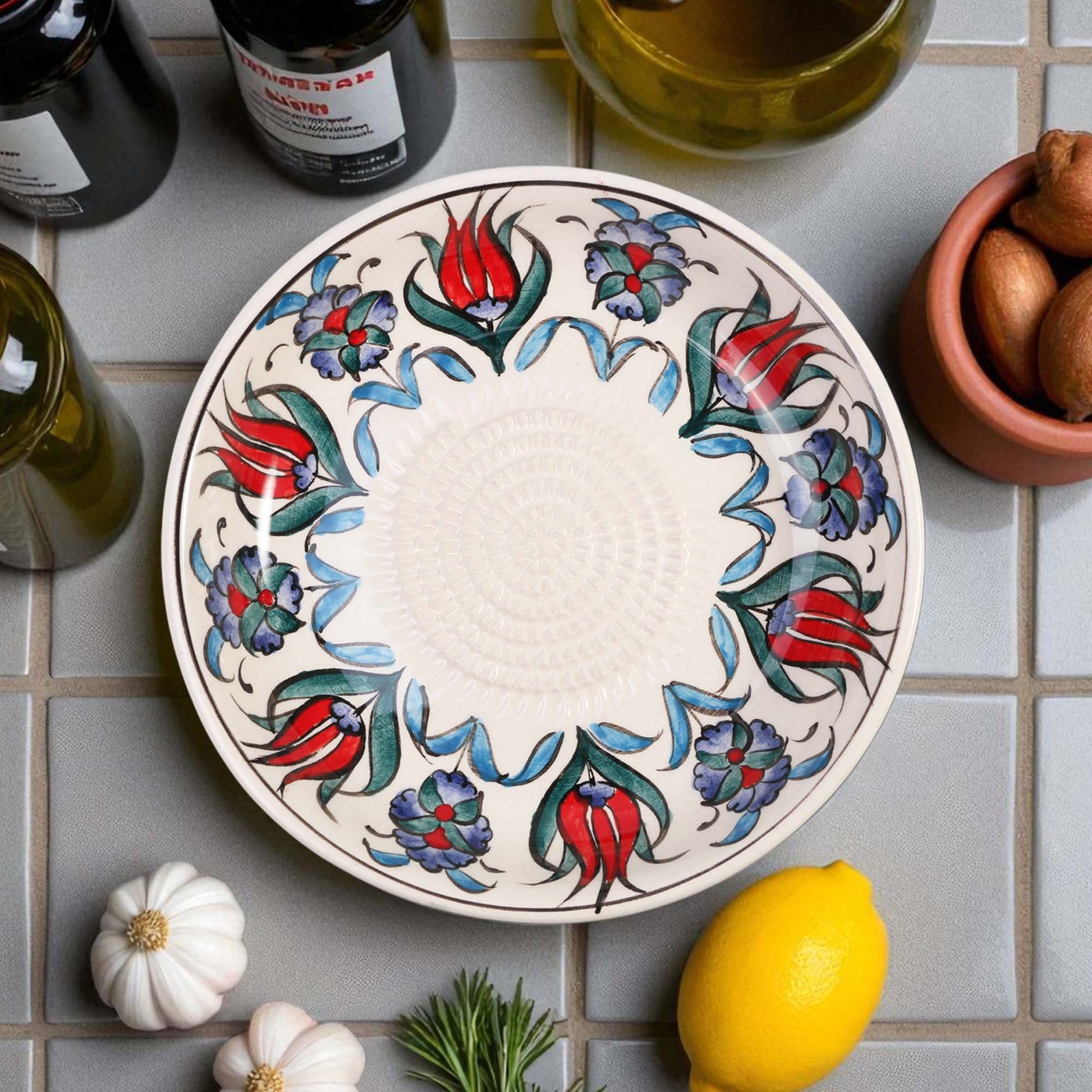 Decorative ceramic garlic grater bowl with floral patterns on a tiled surface with ingredients.