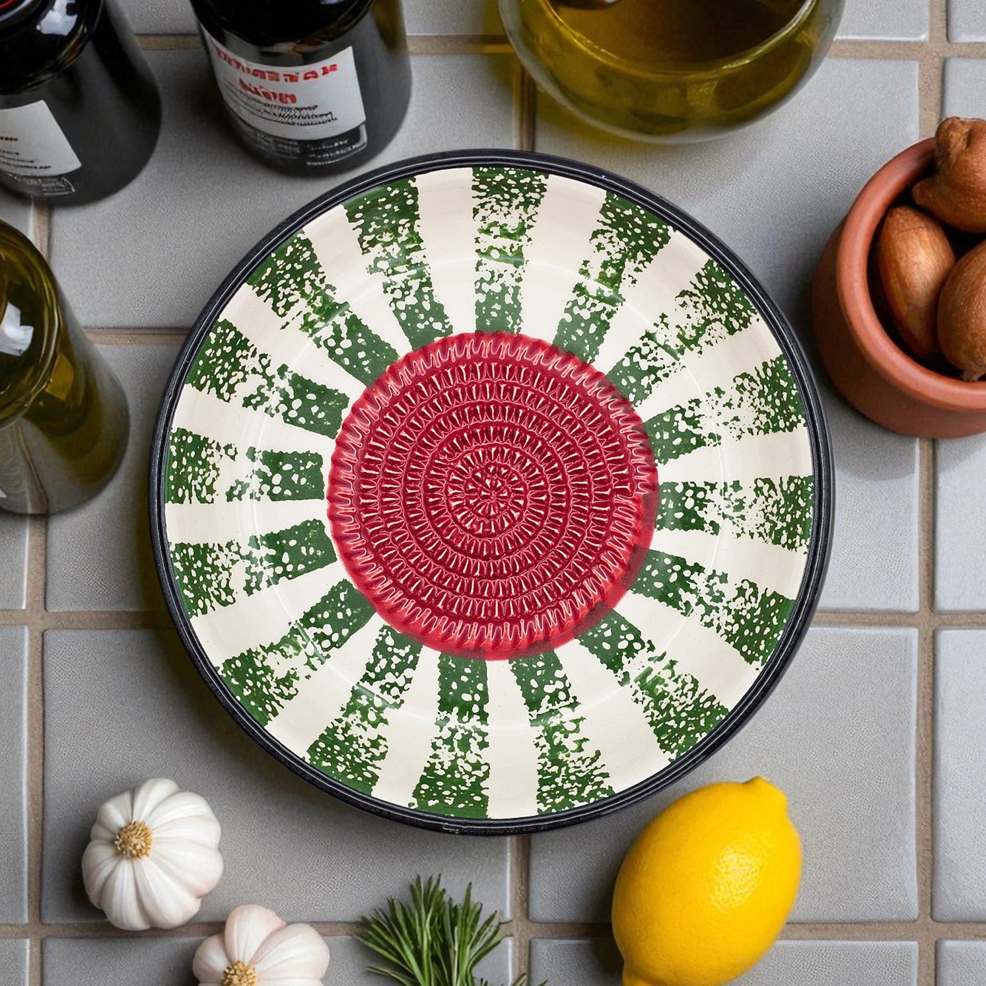 Decorative garlic grater bowl with a red center and green and white pattern on a tiled surface with lemons and herbs.