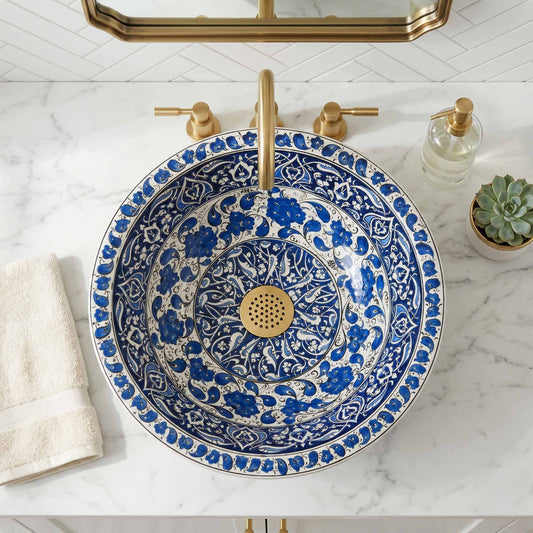 Decorative blue and white sink with gold fixtures on a marble countertop.