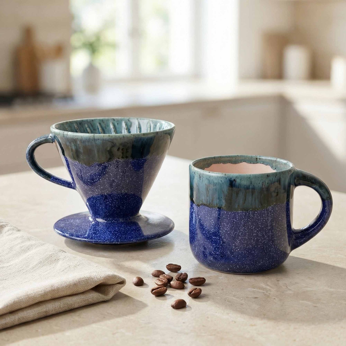 Blue ceramic coffee maker and mug on a kitchen counter with coffee beans.