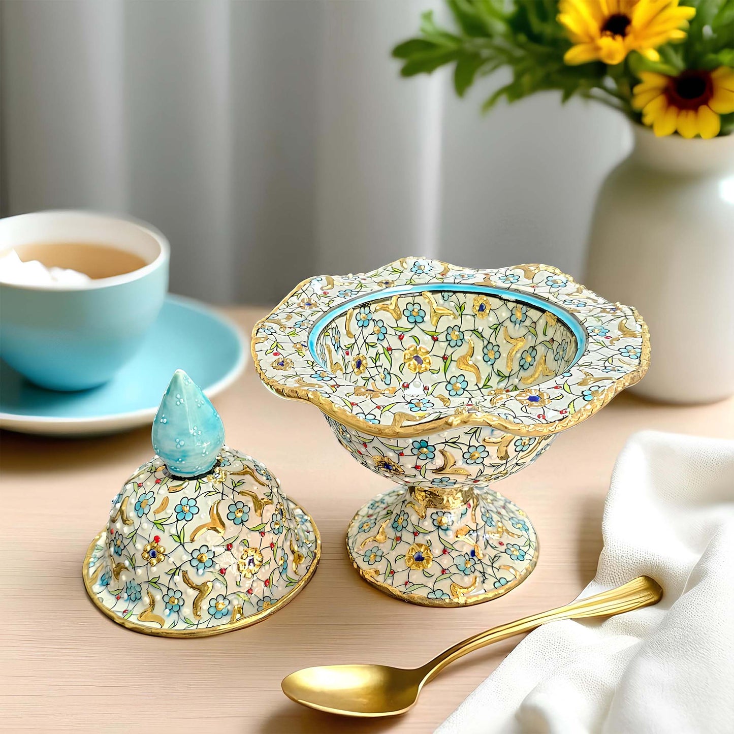 Decorative ceramic sugar bowl with floral patterns on a table with a cup of tea and flowers in the background.
