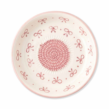 Decorative garlic grater plate with pink bow and circular pattern on a white background